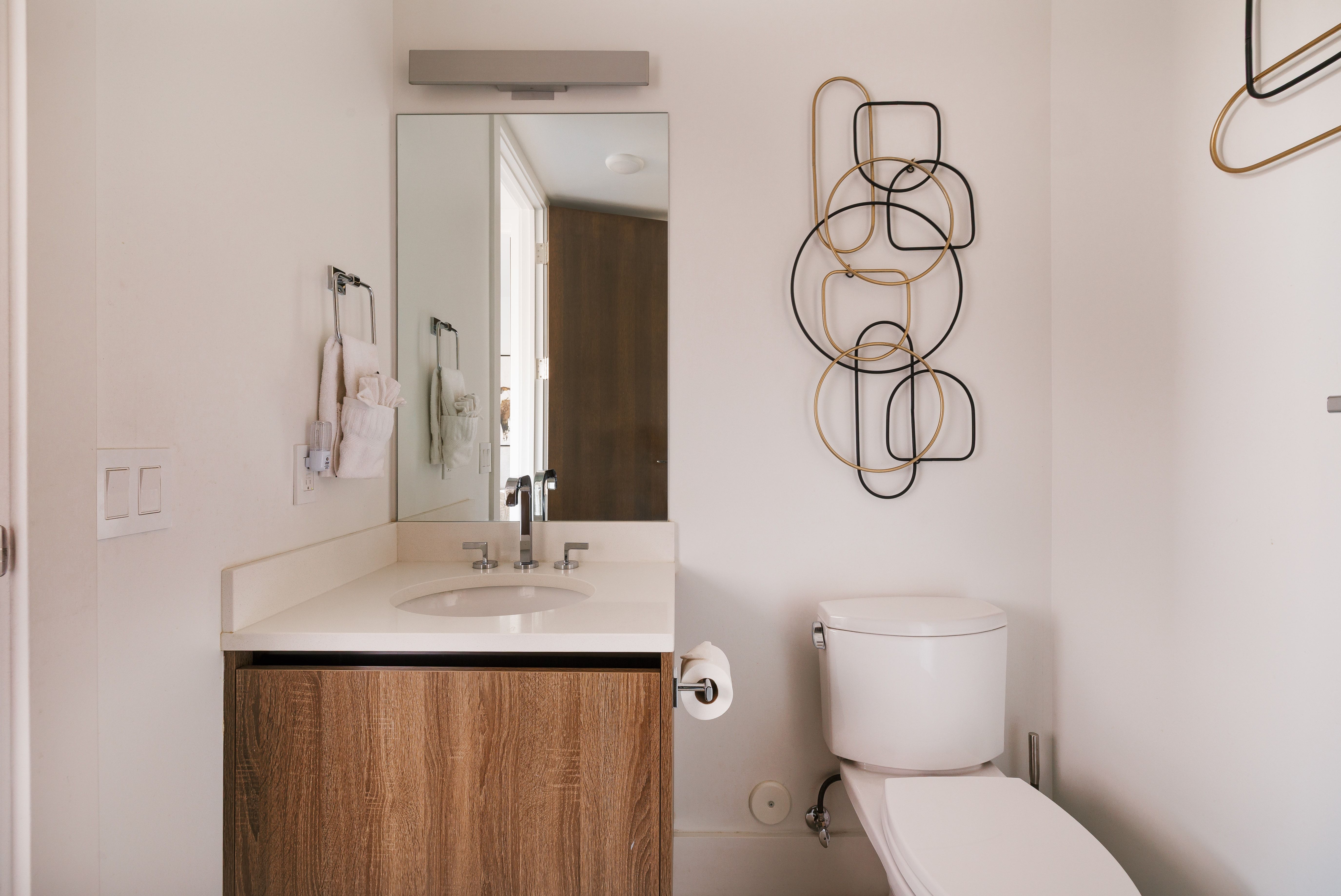 Contemporary bathroom featuring a wood-finish vanity with a single basin sink, white countertop, and modern wall-mounted mirror with overhead lighting