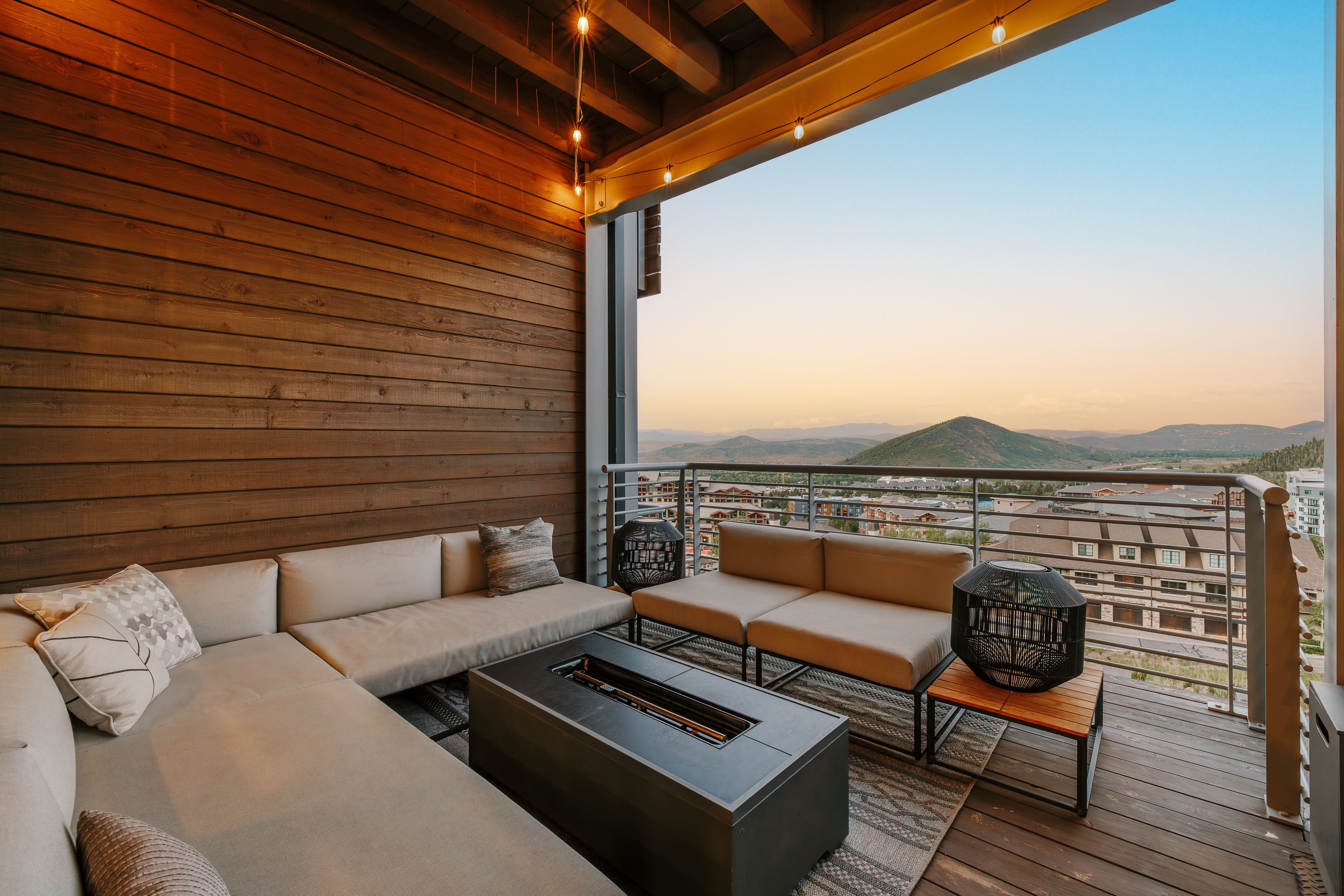 Spacious balcony featuring a wood-plank accent wall, overhead string lighting, and a metal railing system