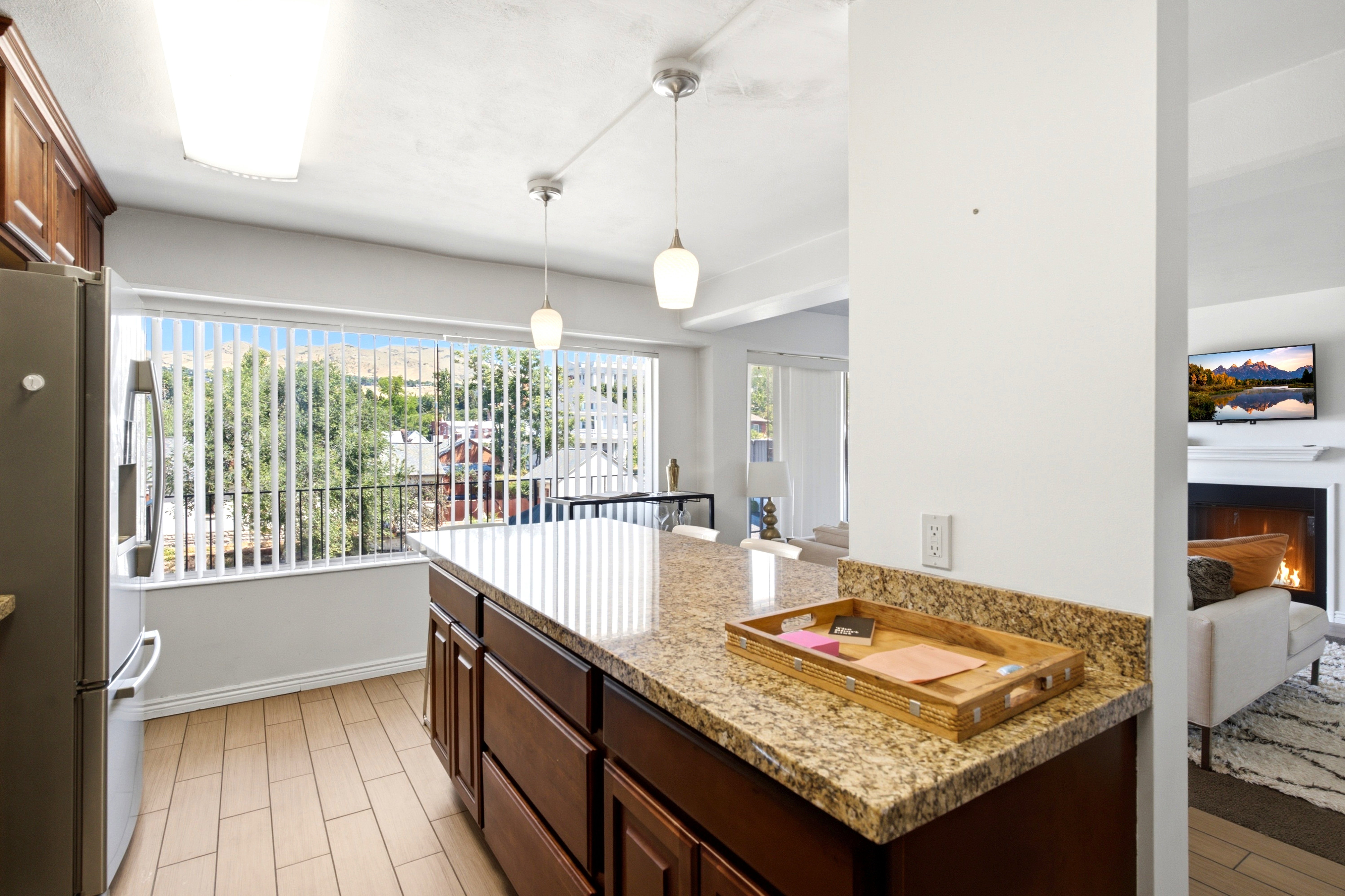 Kitchen featuring a large window with vertical blinds, wood-finish flooring, and a central island with a granite-style countertop and integrated cabinetry