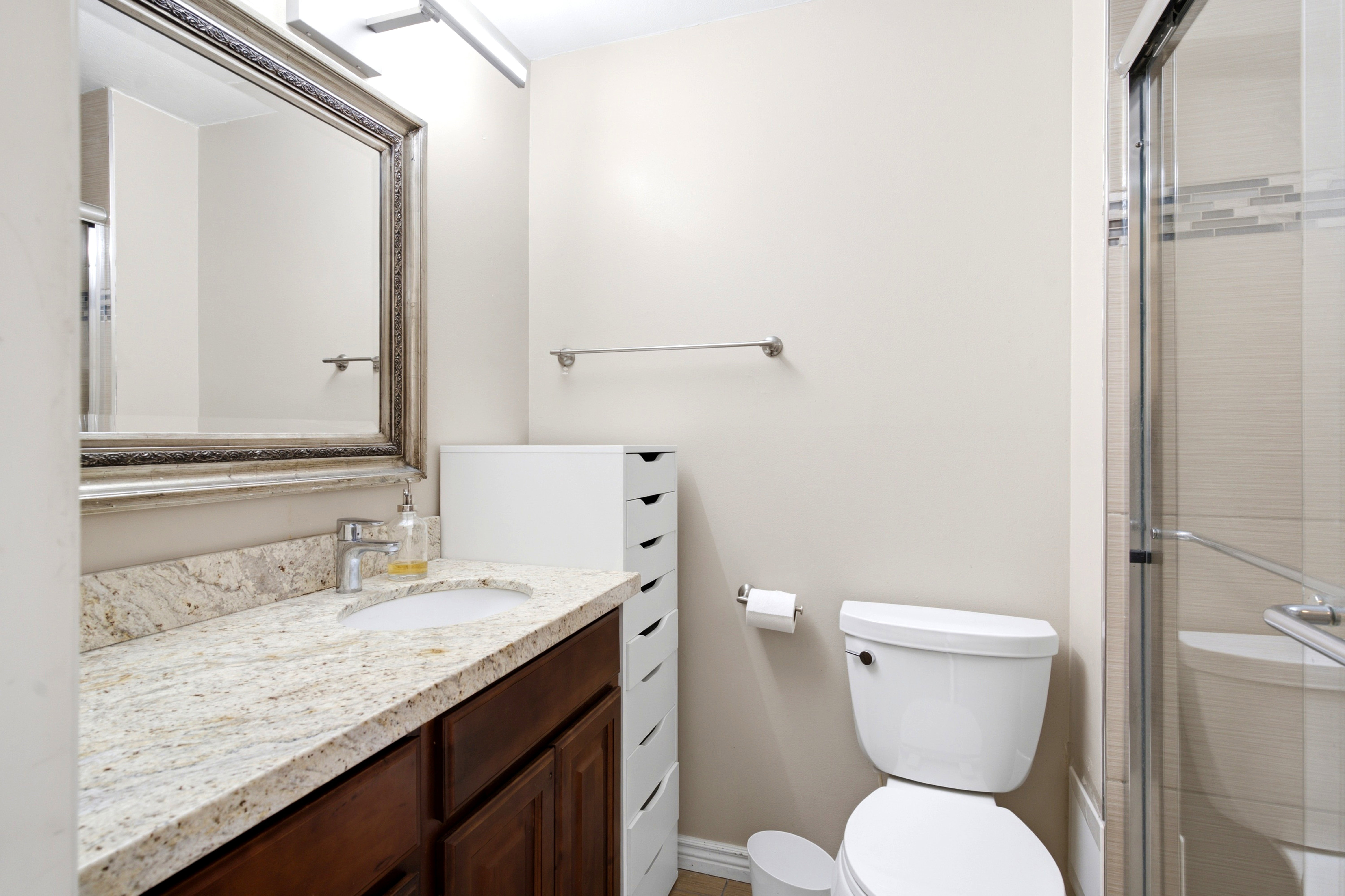Bathroom vanity with a granite countertop, undermount sink, dark wood-finish cabinetry, and a framed mirror