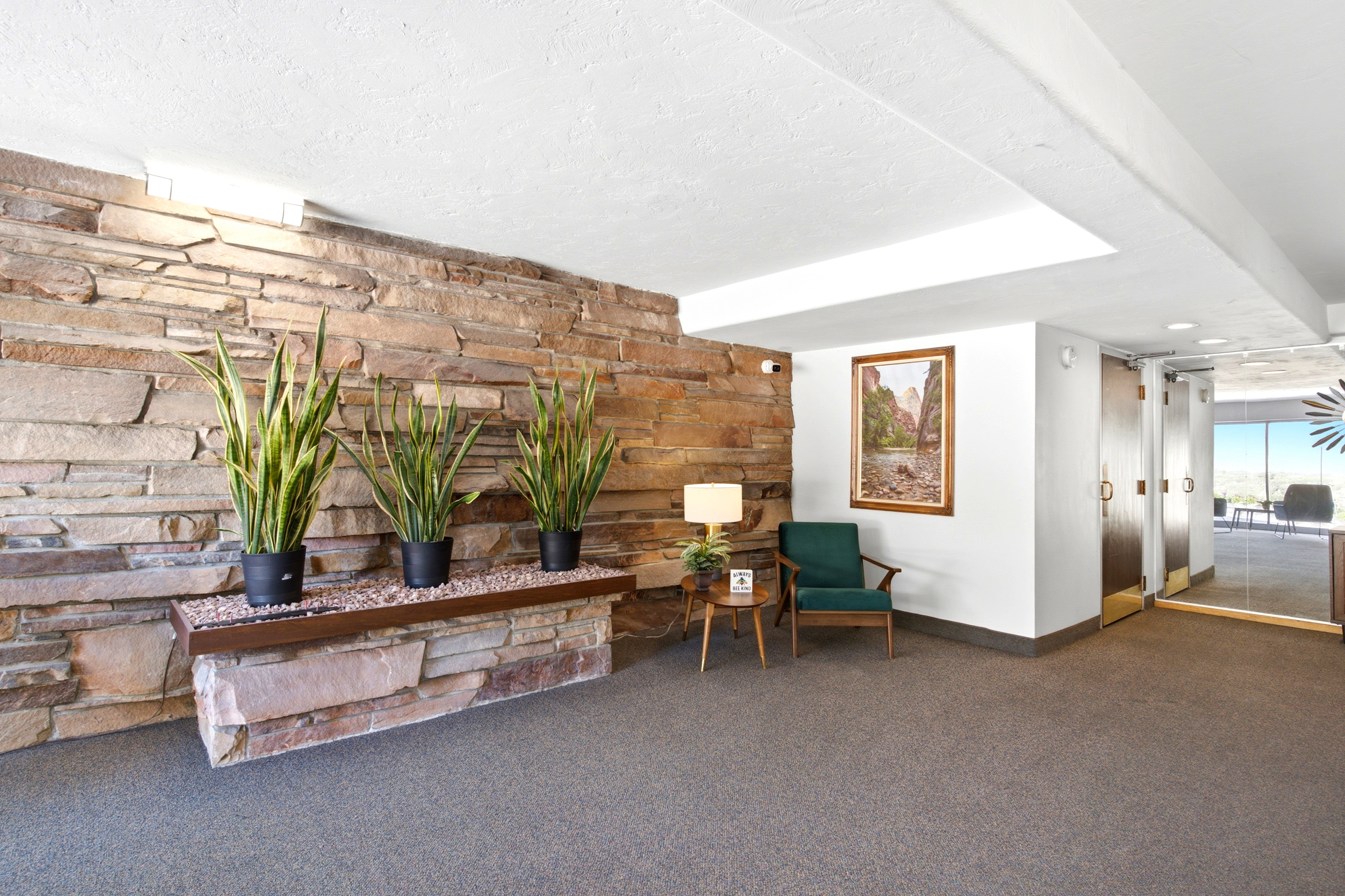 Stone accent wall with integrated planter, neutral carpet flooring, recessed ceiling lighting, and a frosted glass door entrance