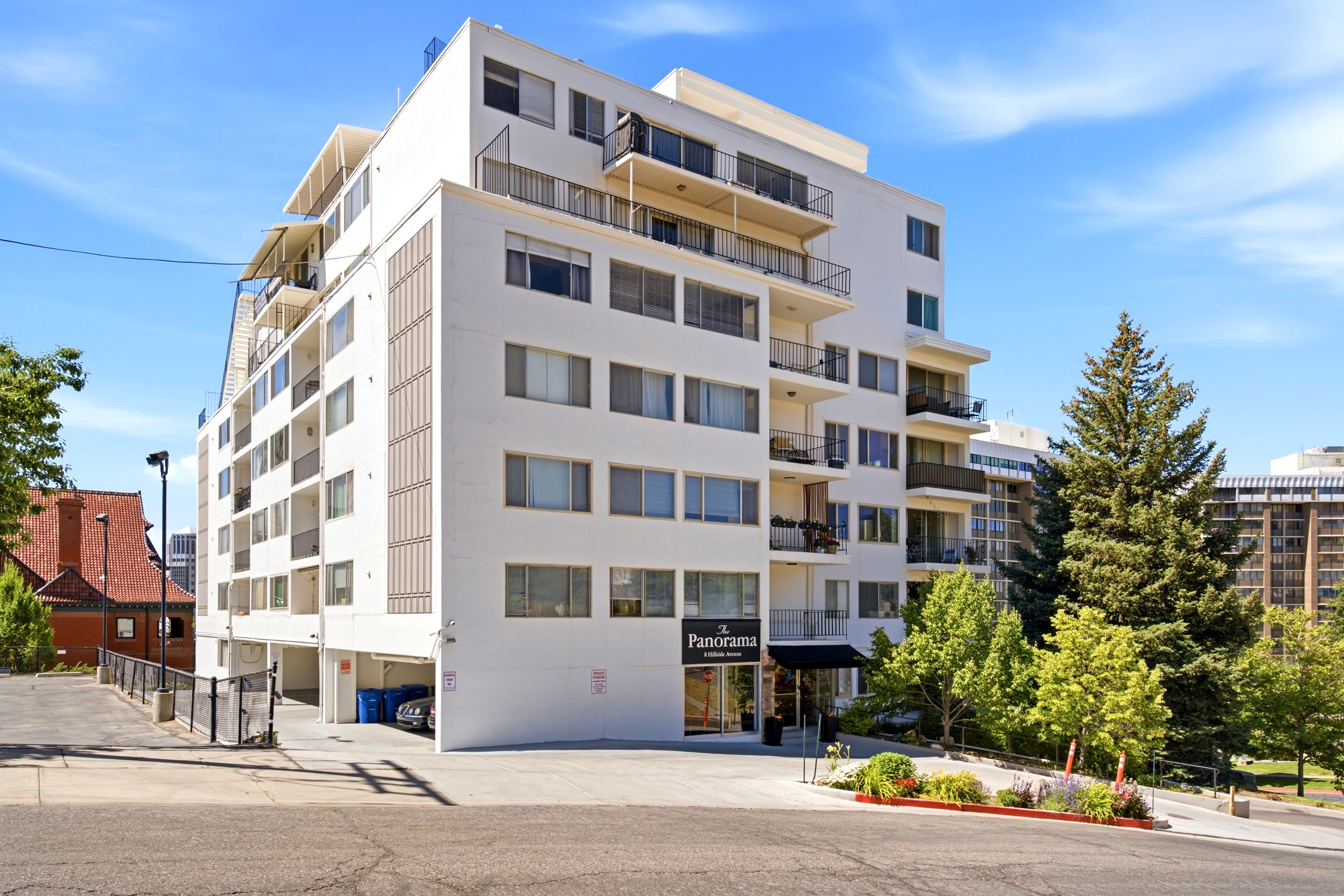 Modern multi-story building featuring a white facade, individual balconies, an entry canopy, and integrated ground-level parking