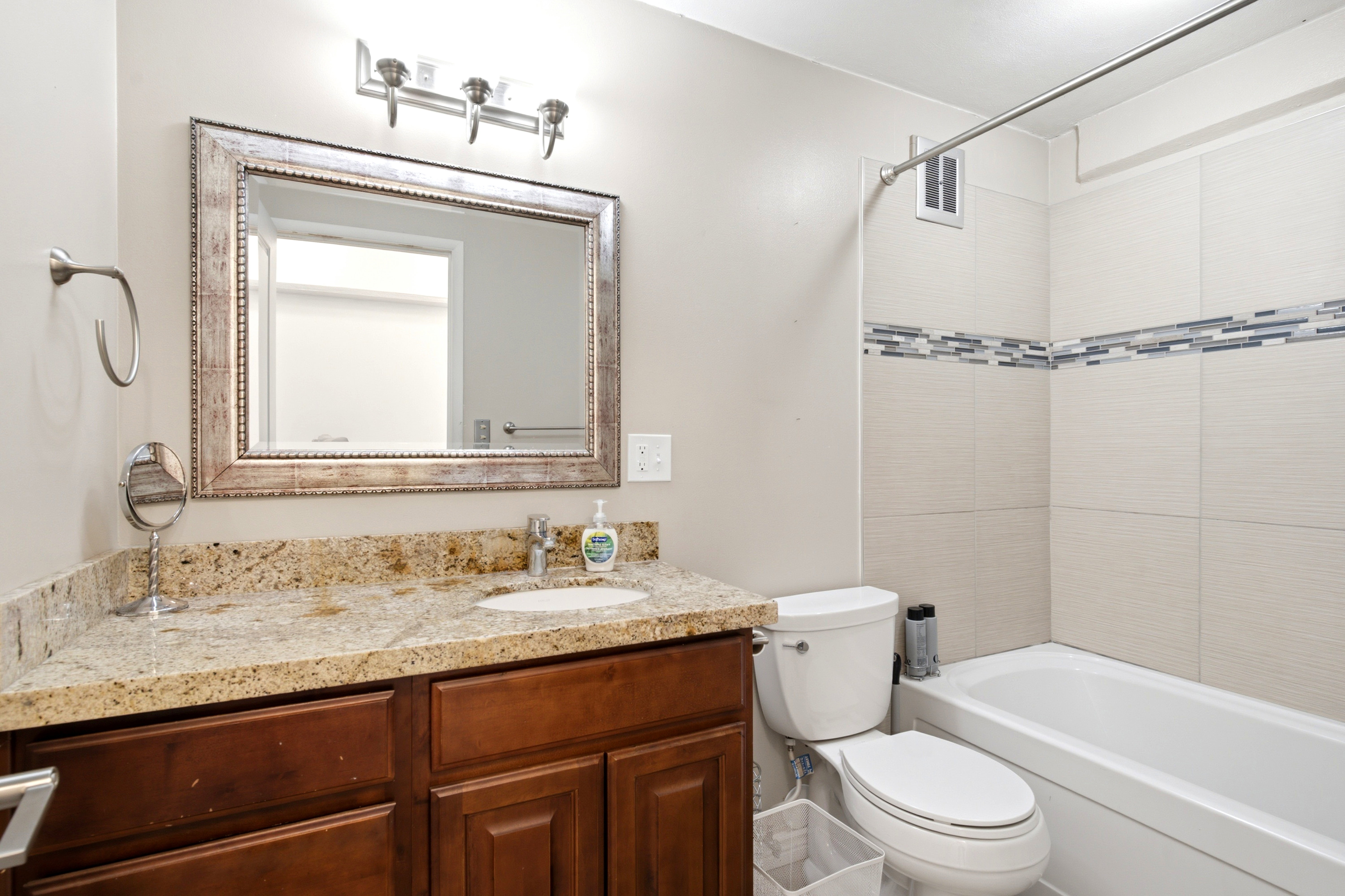 Bathroom featuring a vanity with a granite-style countertop, a rich wood-finish cabinet, and an ornate framed mirror