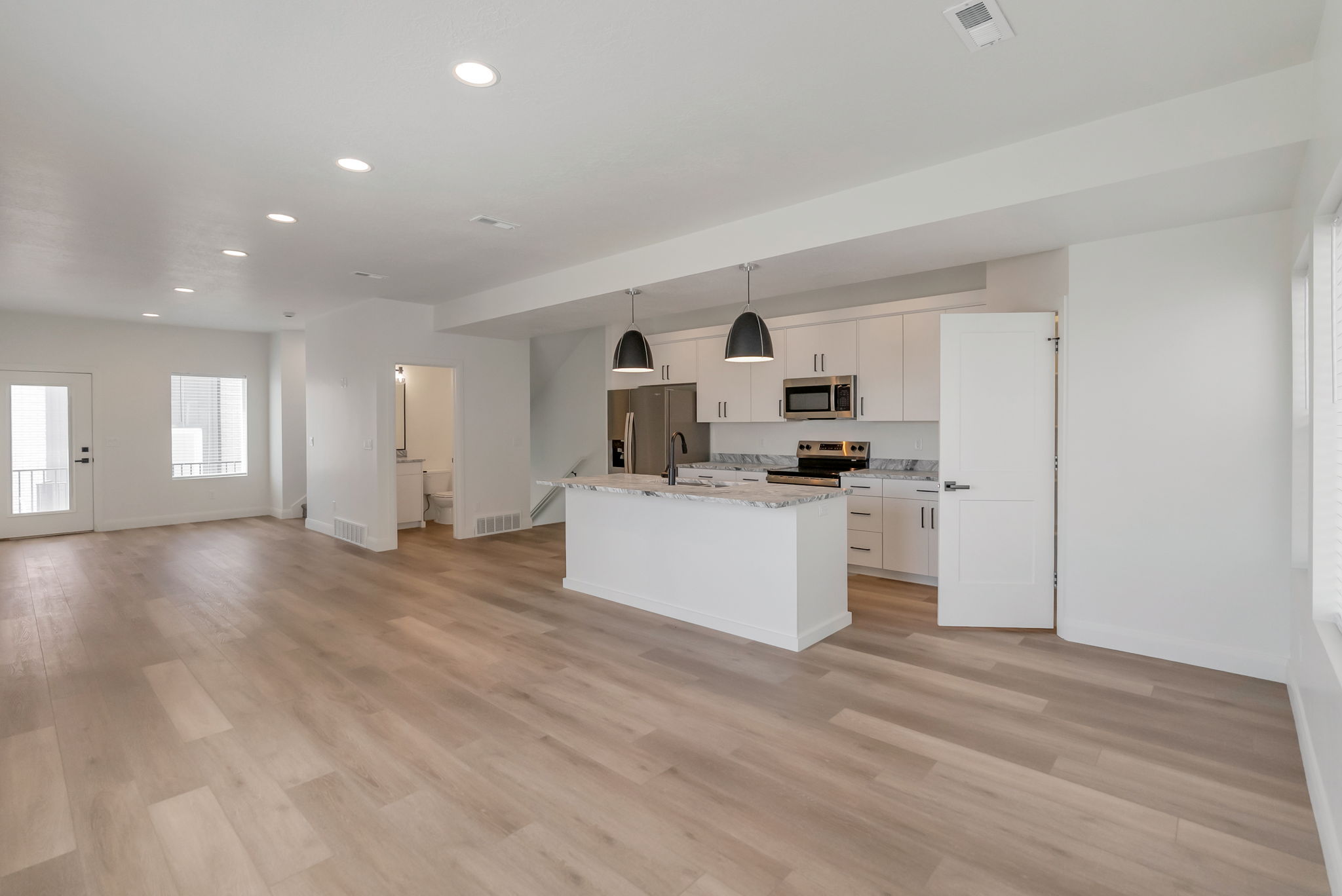 Open-concept living space featuring wood-finish flooring, recessed lighting, and a kitchen with white cabinetry, stainless steel appliances, and a central island with a stone countertop