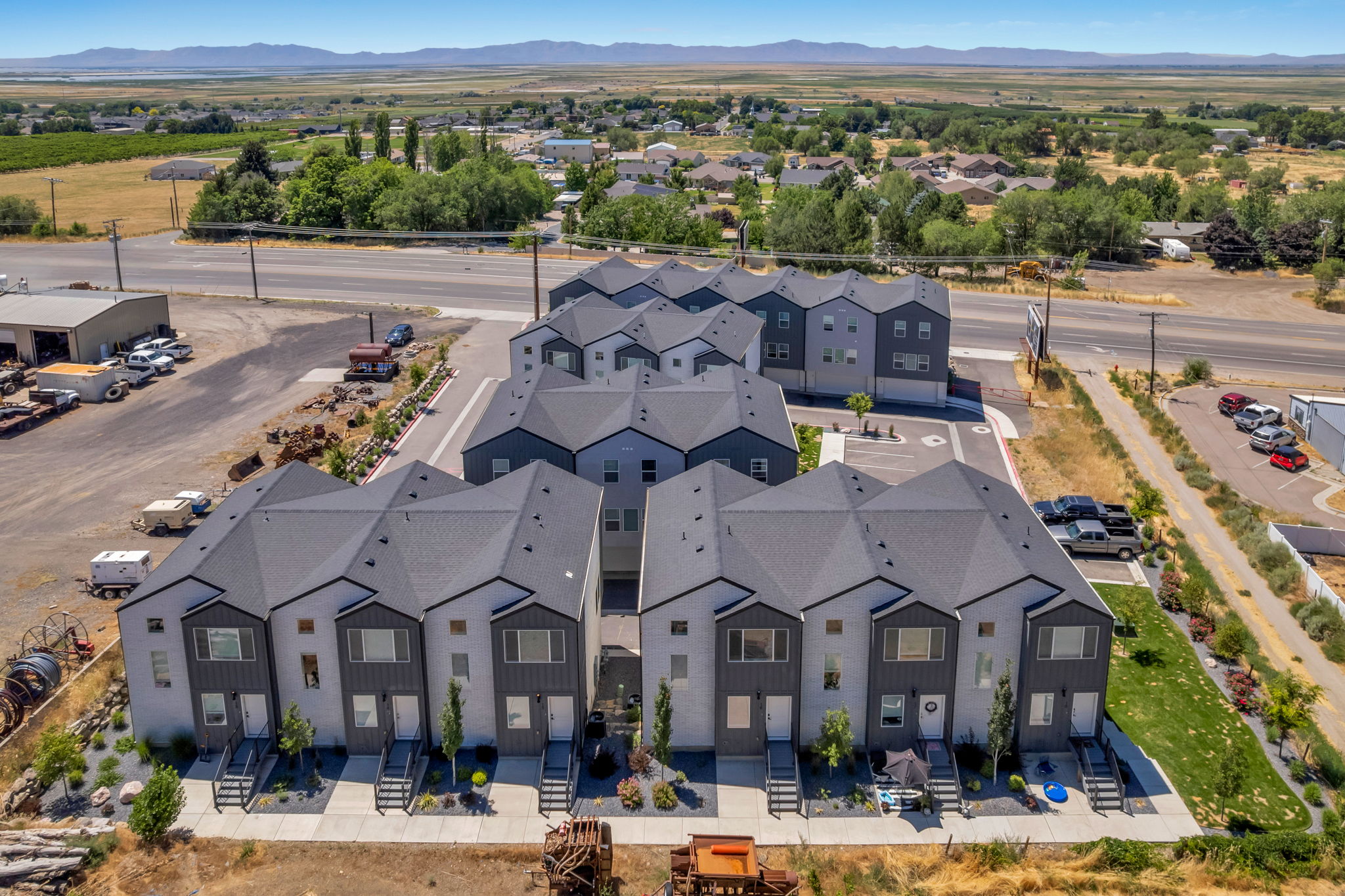 Contemporary townhome development featuring light-colored siding with dark accents, dark pitched roofs, individual front entrances, and integrated landscaping