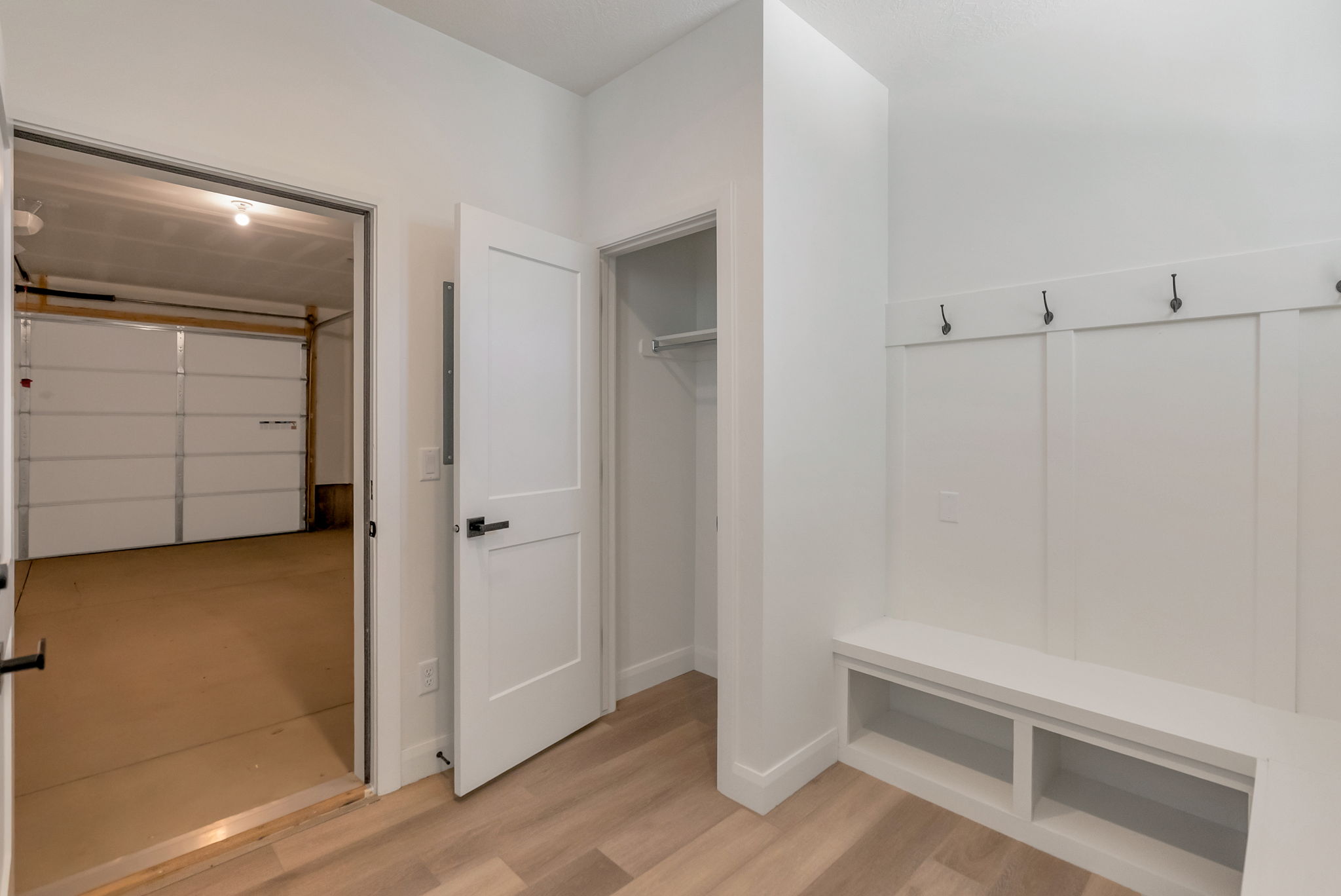Mudroom area featuring built-in bench seating with storage cubbies, a coat rack with four hooks, and wood-finish flooring