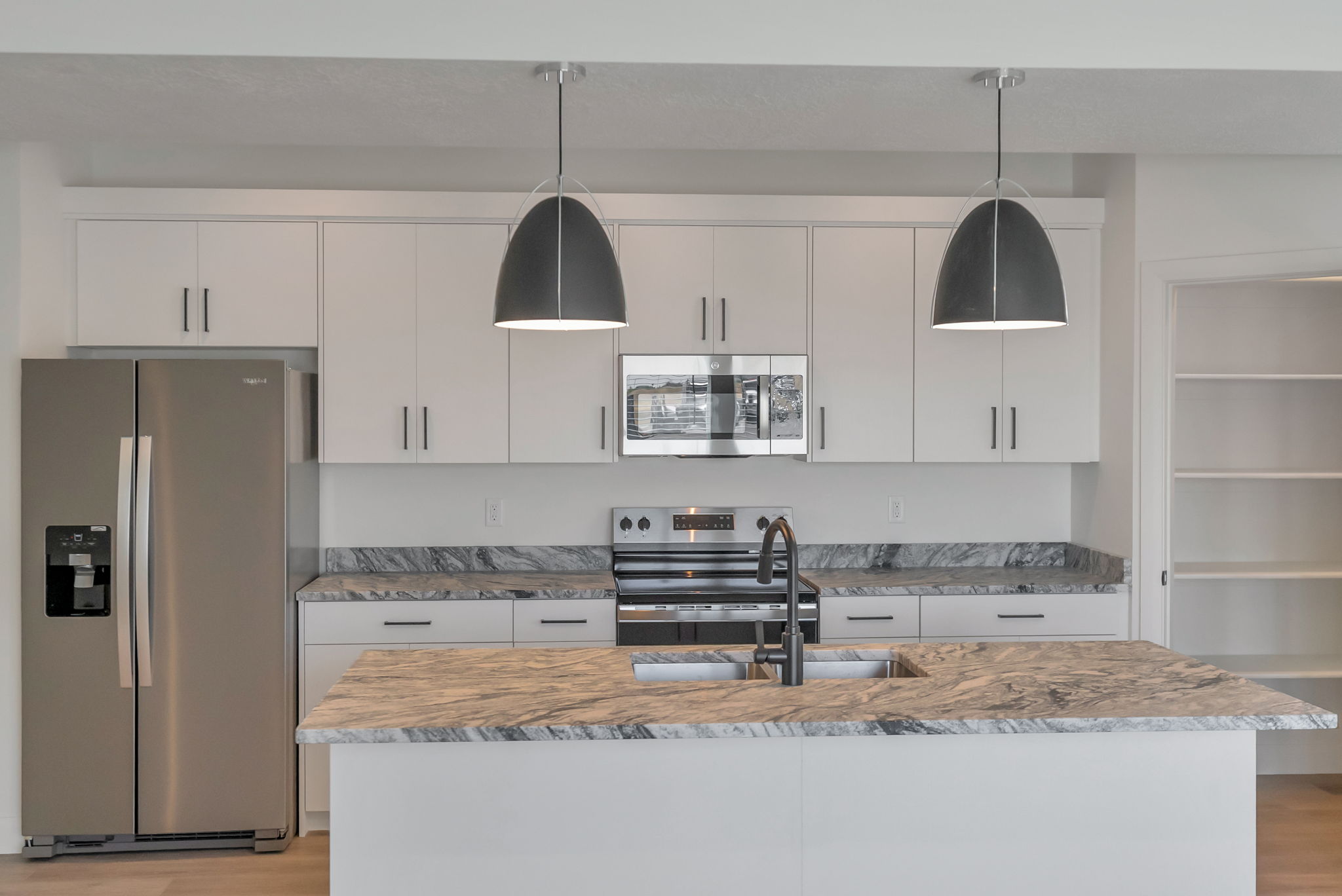Modern kitchen featuring an island with a double basin sink, stainless steel appliances, white cabinetry, and stone countertops