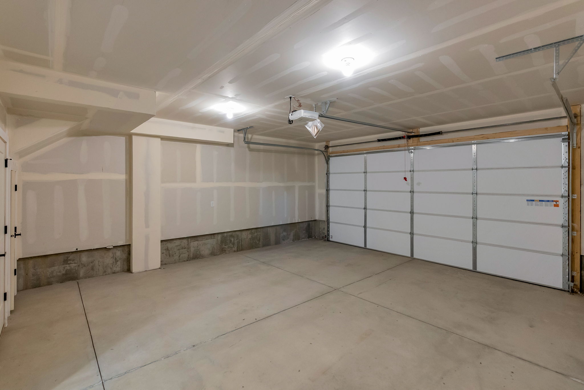 Spacious garage featuring a concrete floor, two overhead light fixtures, exposed ceiling joists, and a sectional garage door