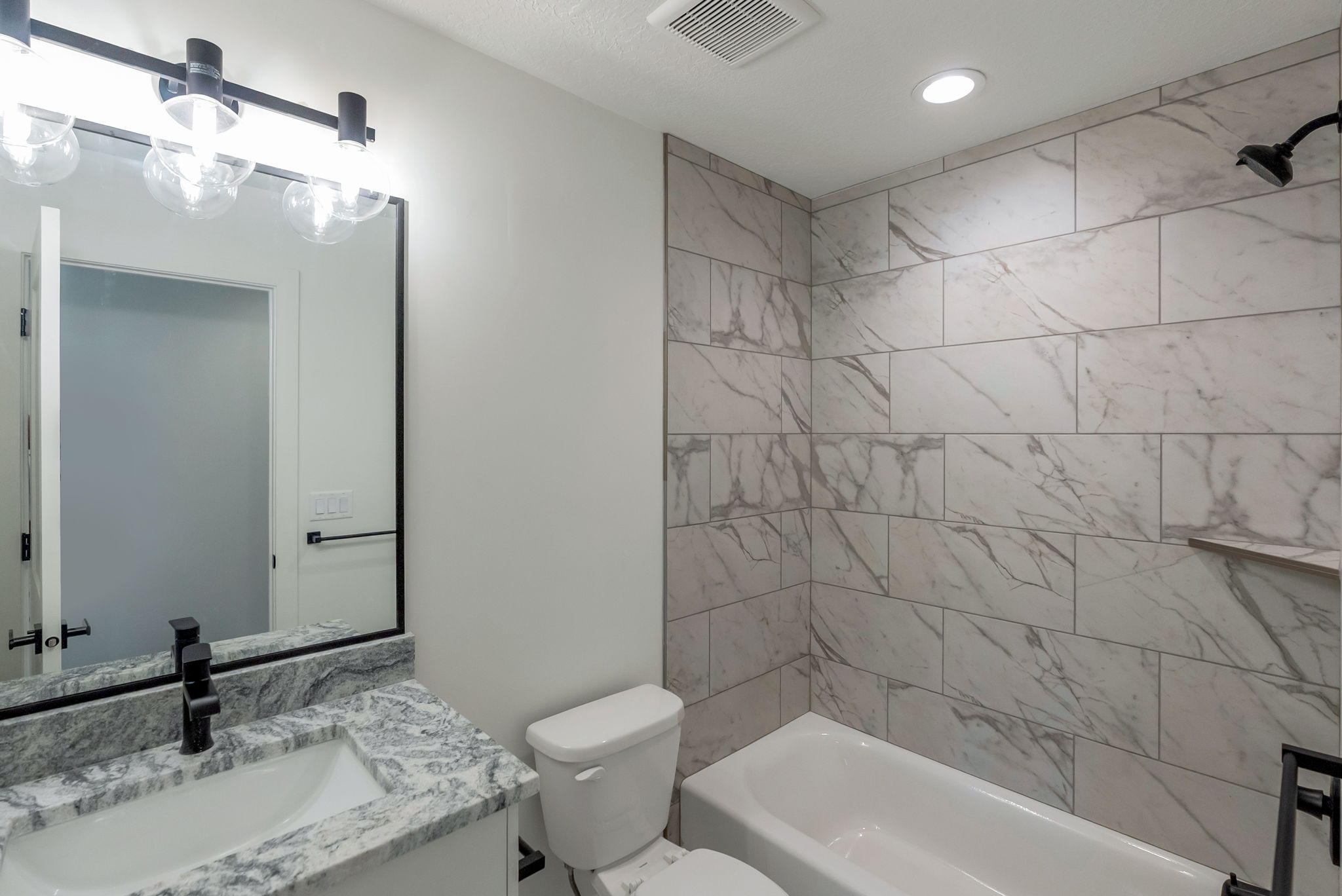 Bathroom featuring a white bathtub, white vanity with a patterned countertop, and a large mirror