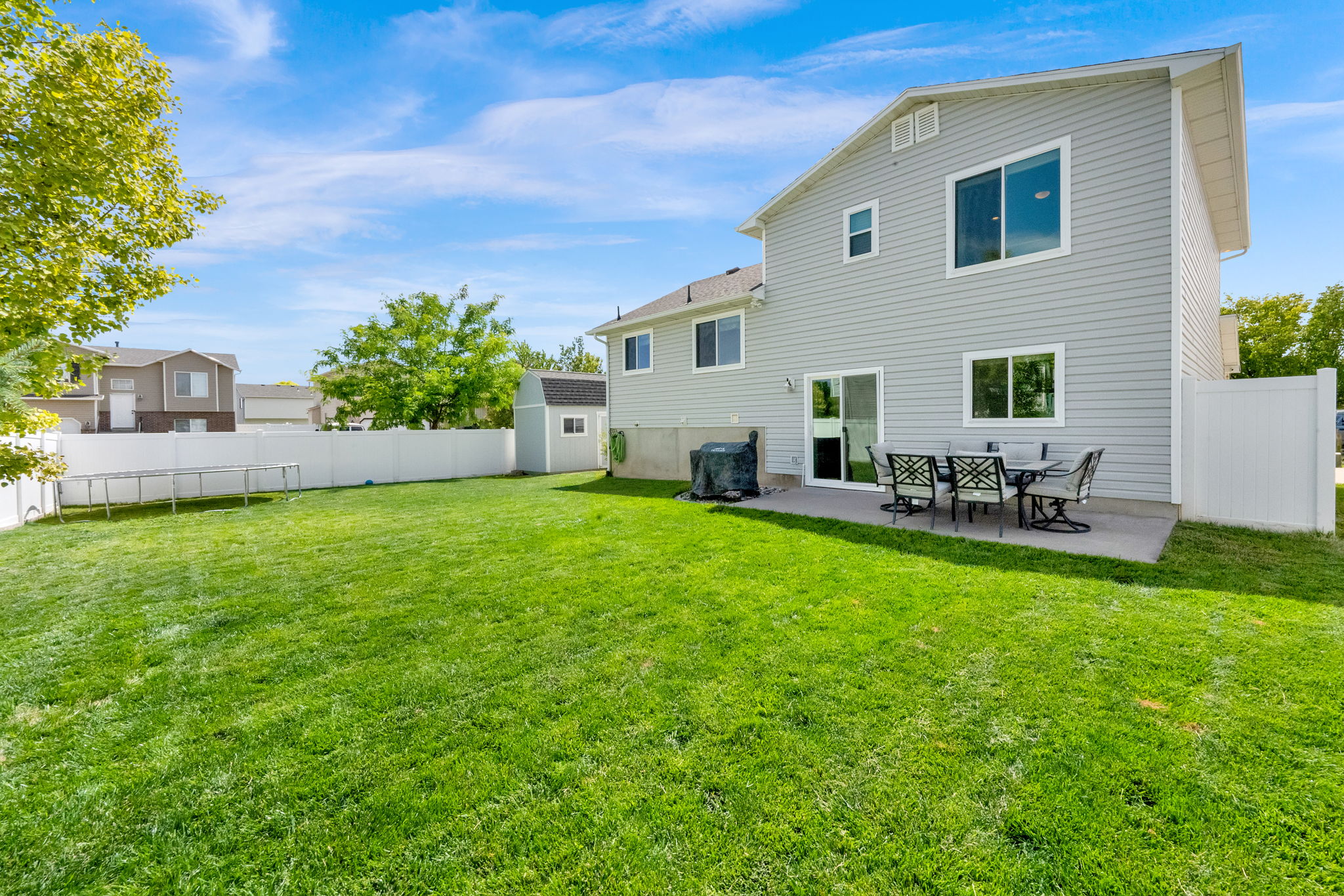 Expansive backyard featuring a manicured lawn, a concrete patio, and a storage shed