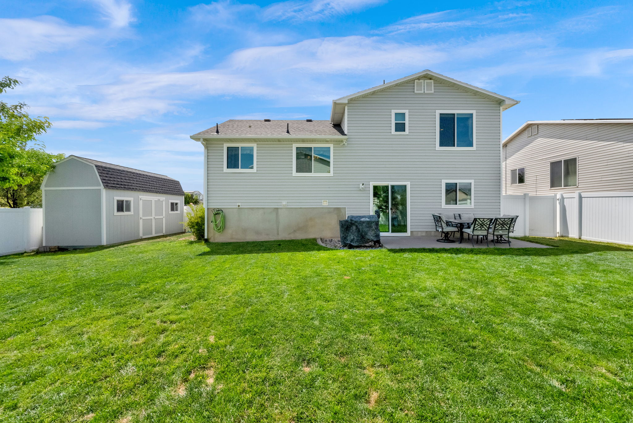 Spacious backyard featuring a large green lawn, a concrete patio, and a light gray two-story siding exterior
