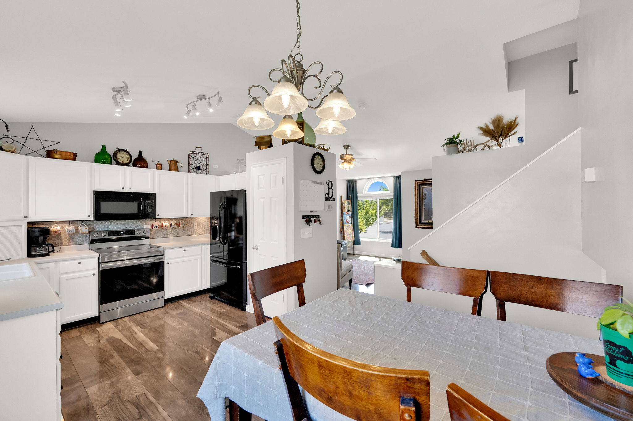Open-concept kitchen and dining area featuring white cabinetry, stainless steel appliances, wood-finish flooring, and a decorative chandelier