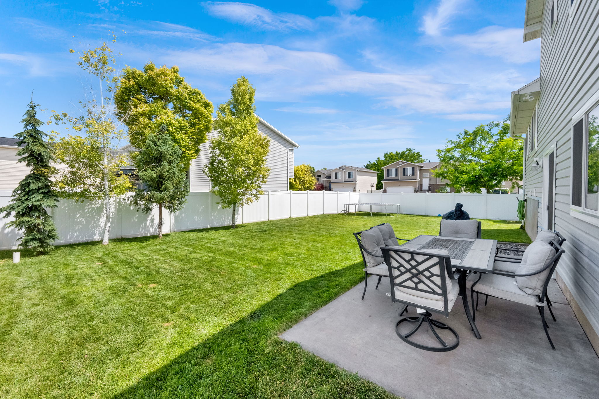 Expansive green lawn featuring a concrete patio, mature trees, and a white privacy fence