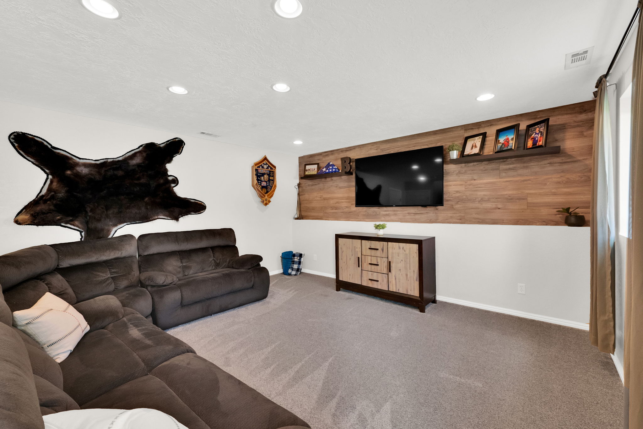 Recessed lighting illuminates the carpeted floor and accent wall with wood-finish paneling