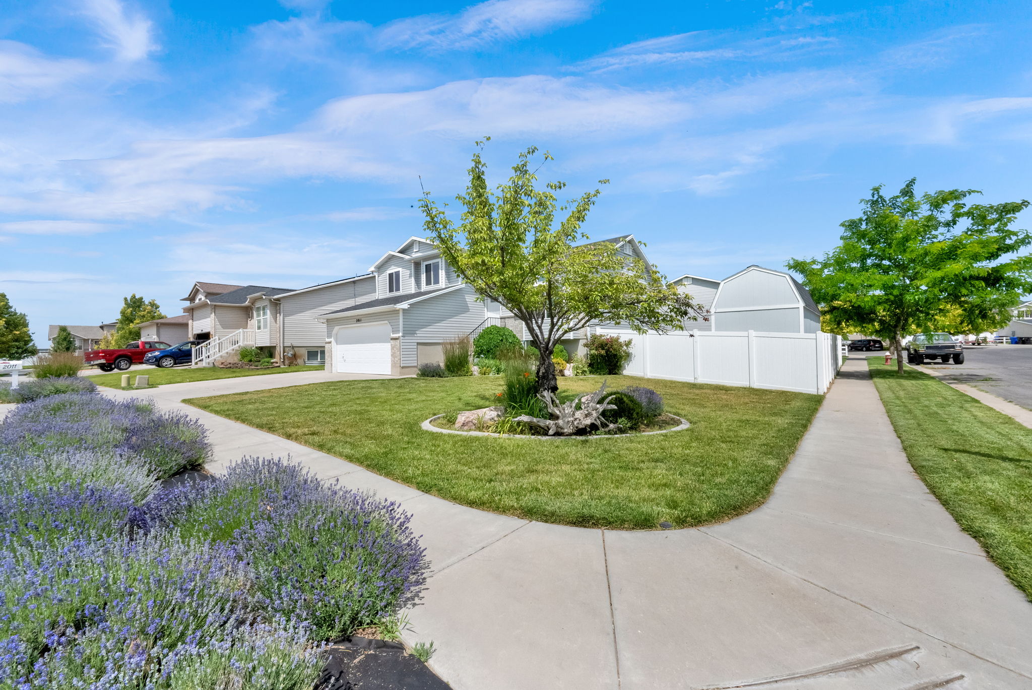 Exterior residence featuring light gray siding, an attached two-car garage, and a white vinyl privacy fence