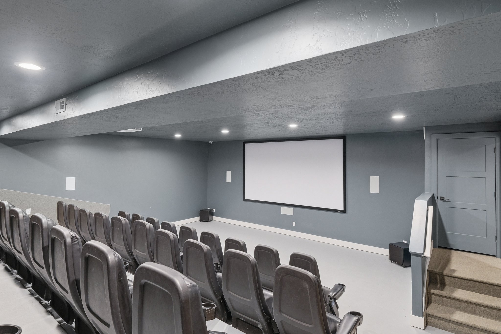 Dedicated home theater featuring tiered seating, a large projection screen, recessed lighting, and wall-mounted speakers