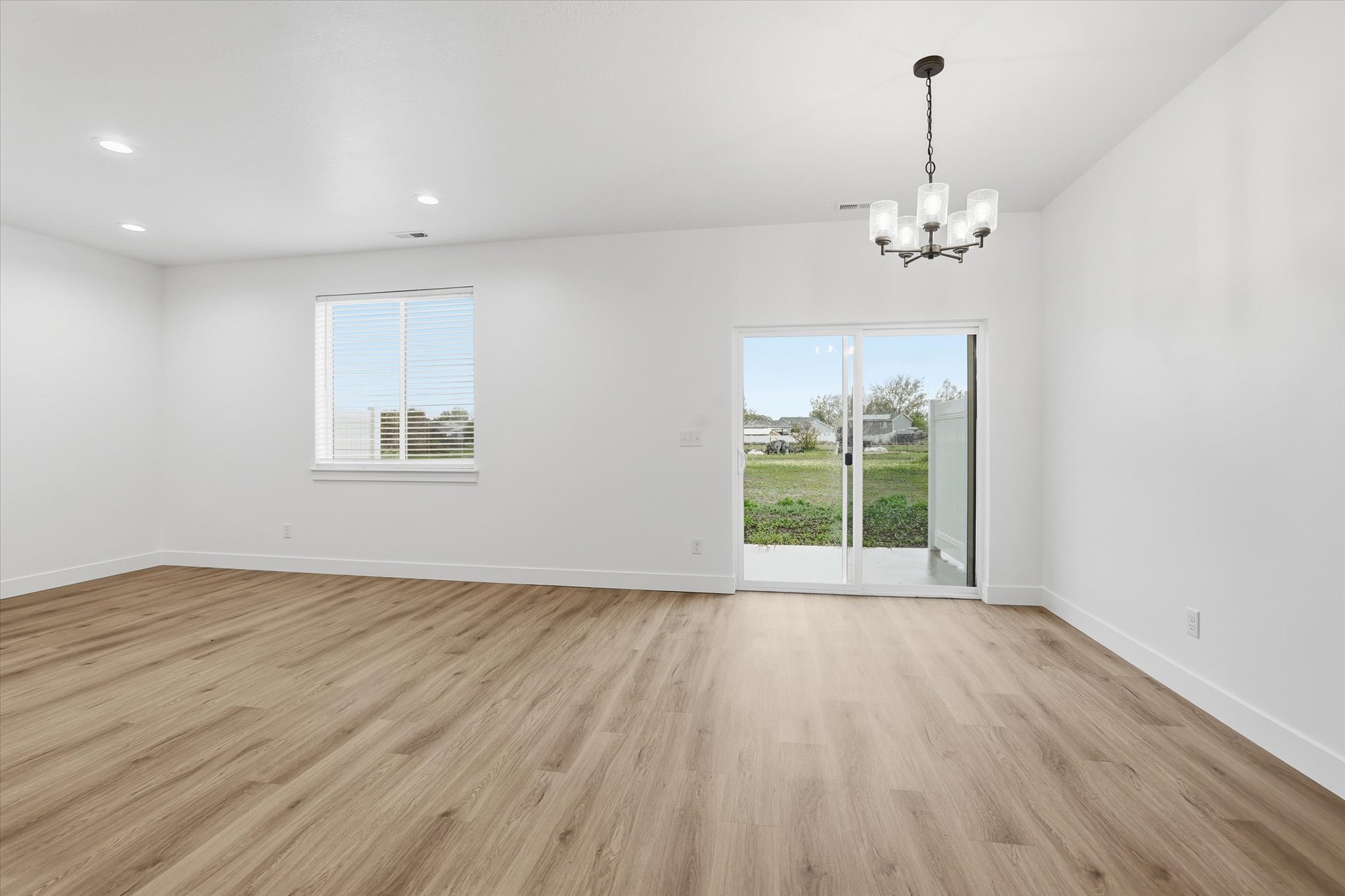 Spacious interior featuring wood-finish flooring, white walls, and a contemporary chandelier