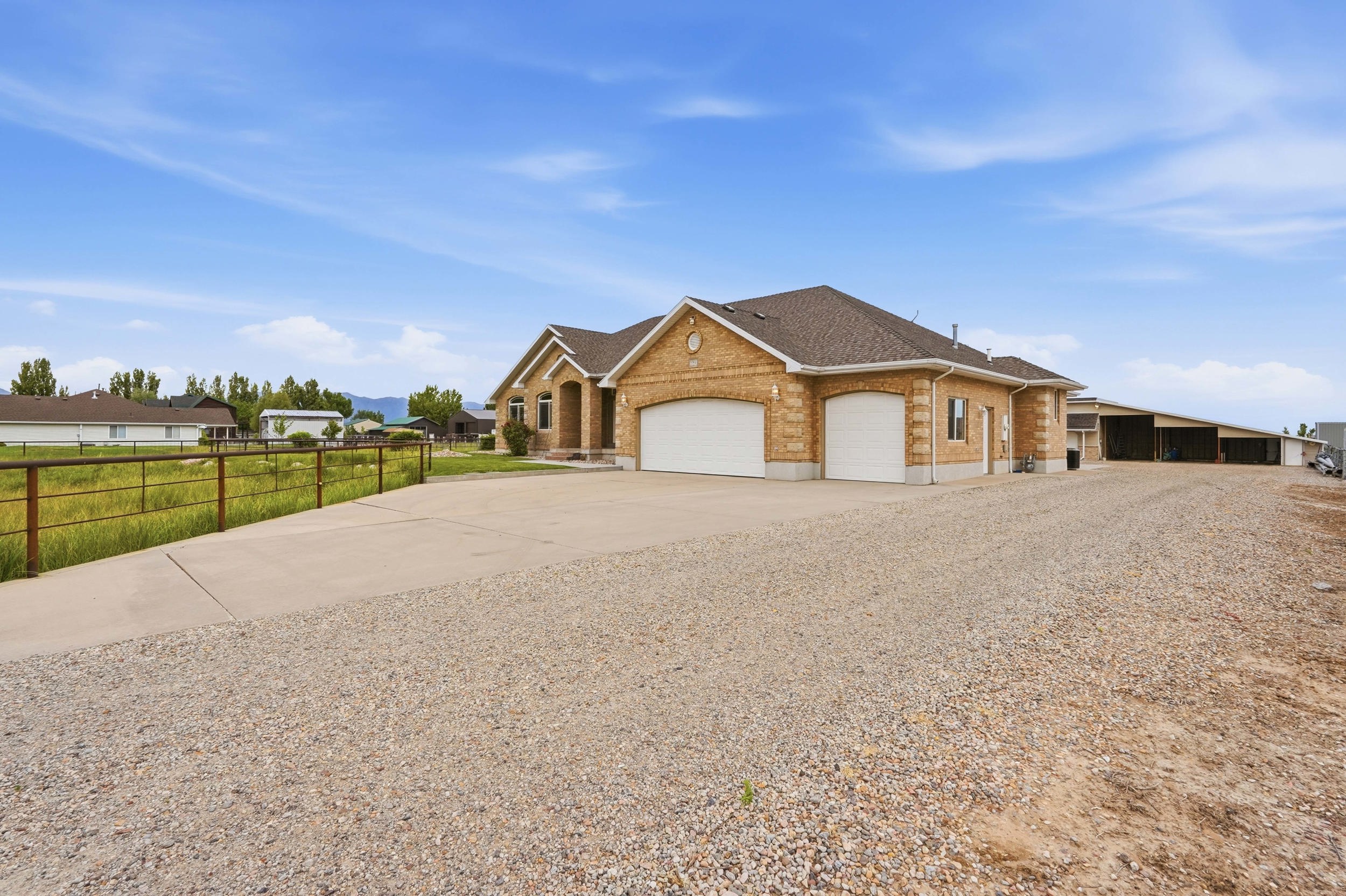 Brick exterior ranch-style residence featuring a two-car garage, expansive gravel driveway, and a concrete approach