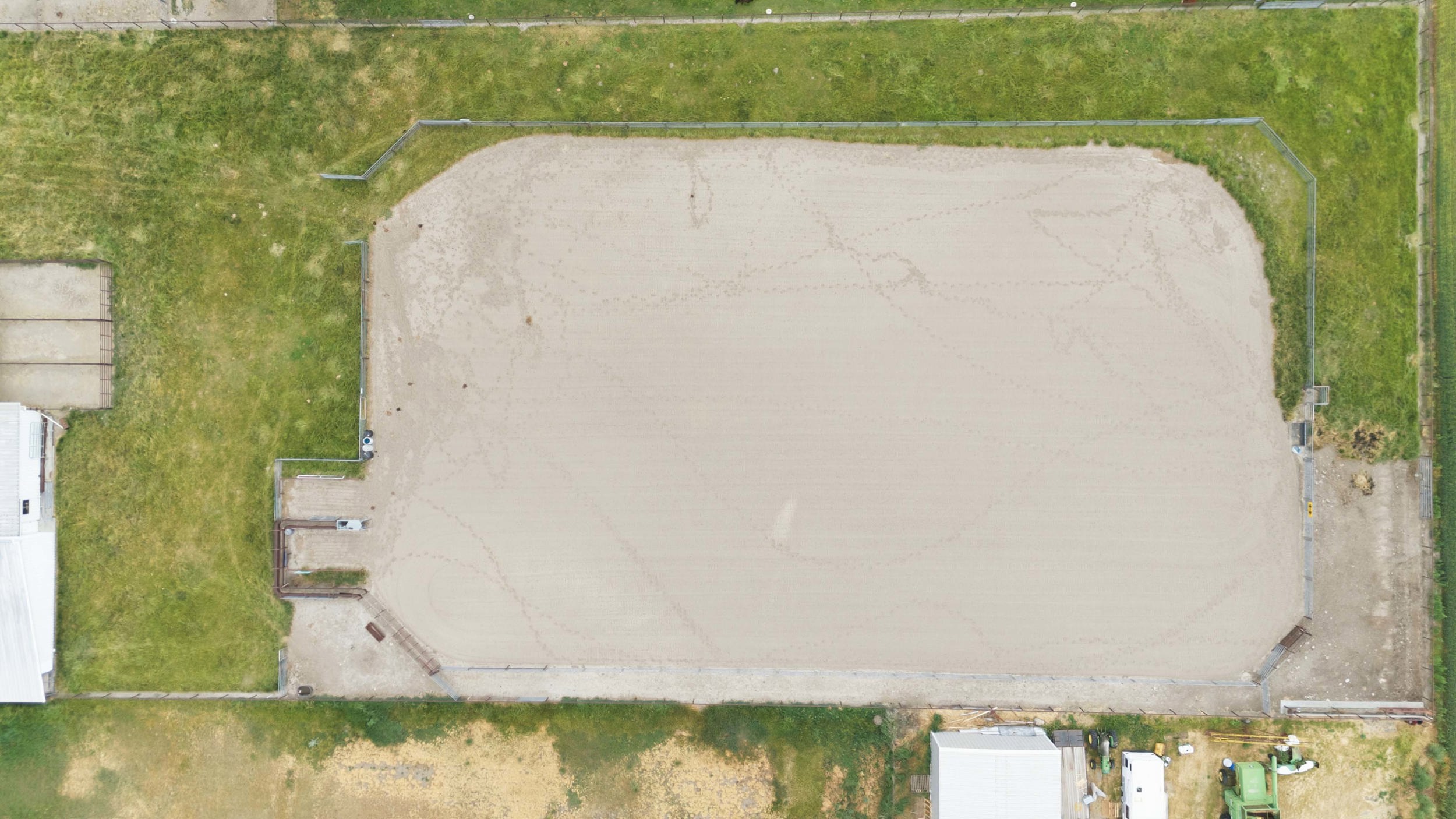 Expansive sand arena with perimeter fencing, surrounded by green space