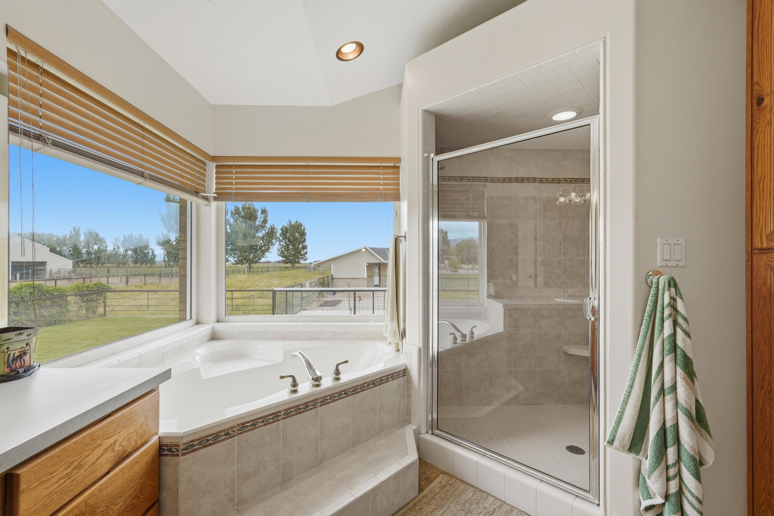 Soaking tub with tile surround and large picture windows, featuring an adjacent glass-enclosed shower with tiled walls and a built-in bench