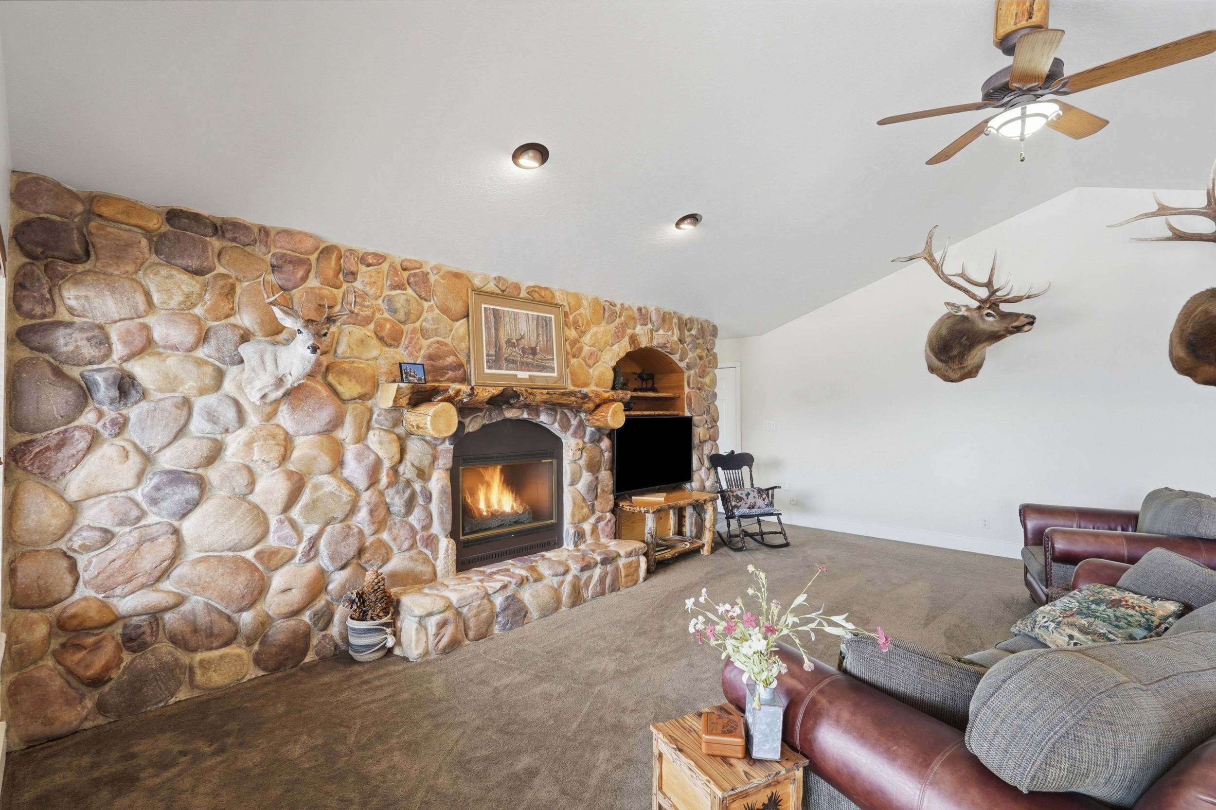 Spacious living area featuring a floor-to-ceiling river rock fireplace with a stone hearth, natural wood mantle, and built-in shelving