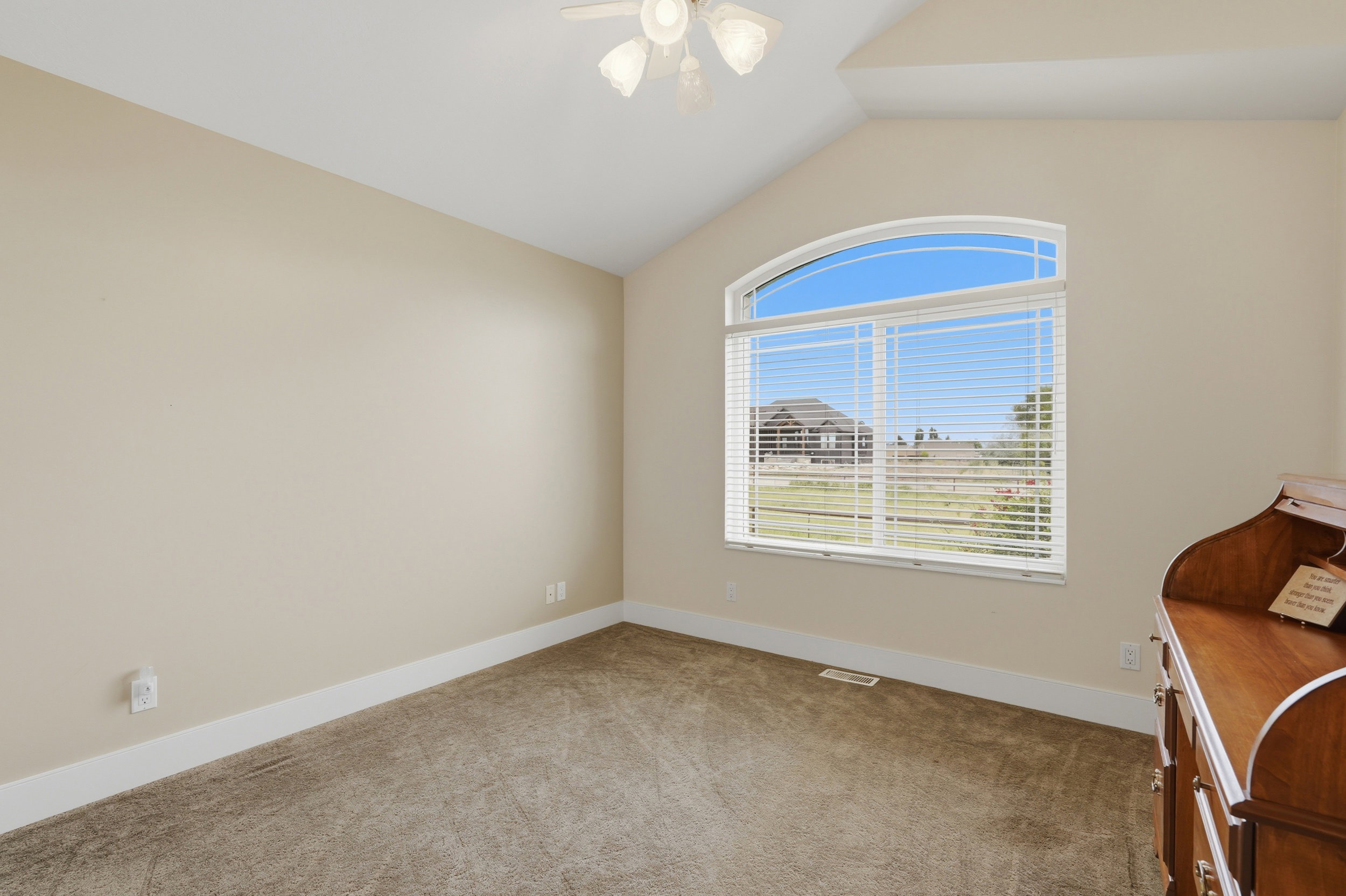 Vaulted ceiling room featuring an arched window, textured carpet flooring, and a ceiling fan with light fixture