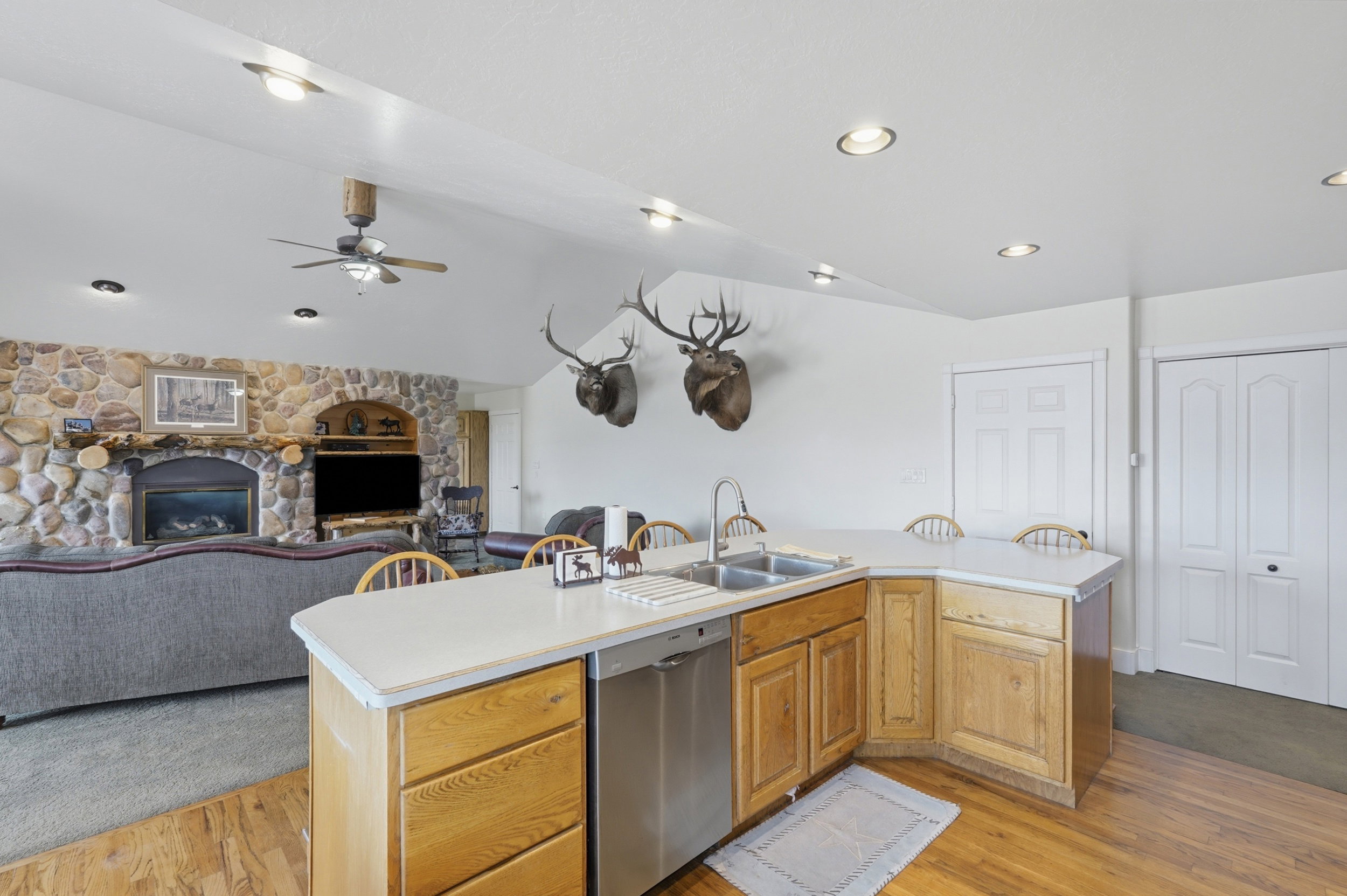 Open-concept living space featuring a kitchen island with integrated sink, wood-finish flooring, and a stone-clad fireplace