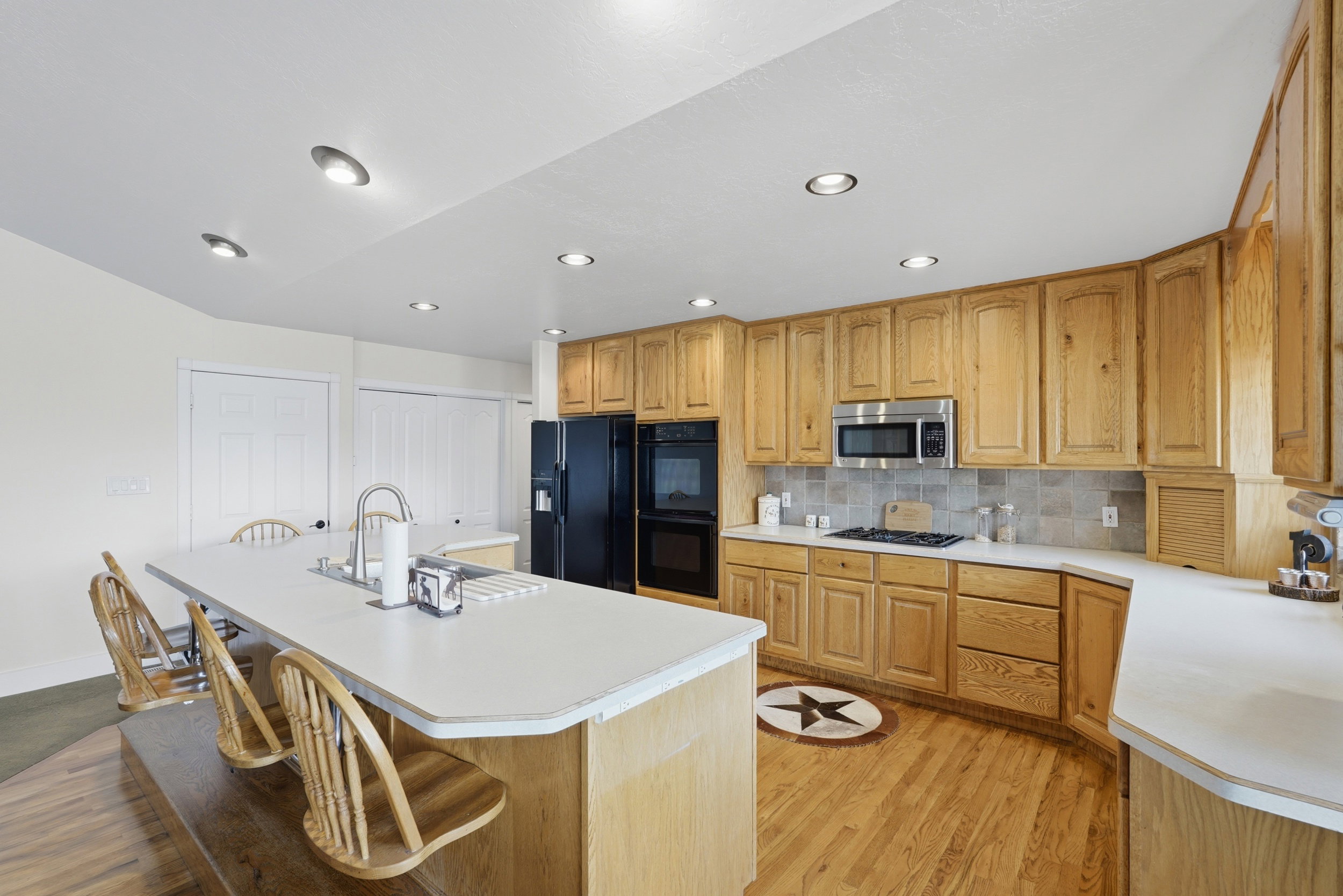 Kitchen featuring an expansive island with an integrated sink, ample natural wood cabinetry, a built-in microwave, black appliances, and recessed lighting
