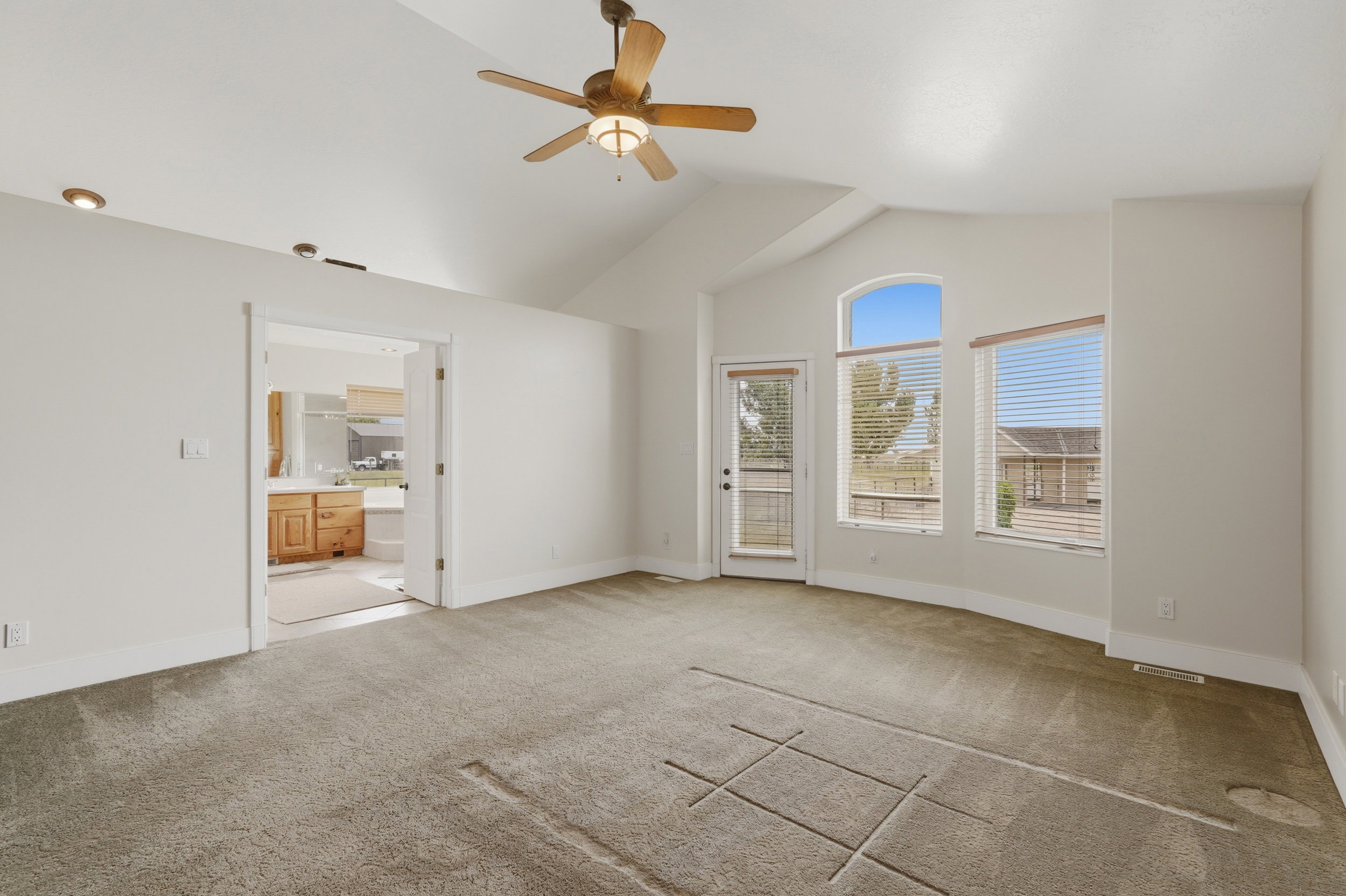 Spacious room featuring vaulted ceilings, a ceiling fan with integrated lighting, recessed lighting, and a glass-paneled exterior door with side windows including an arched transom