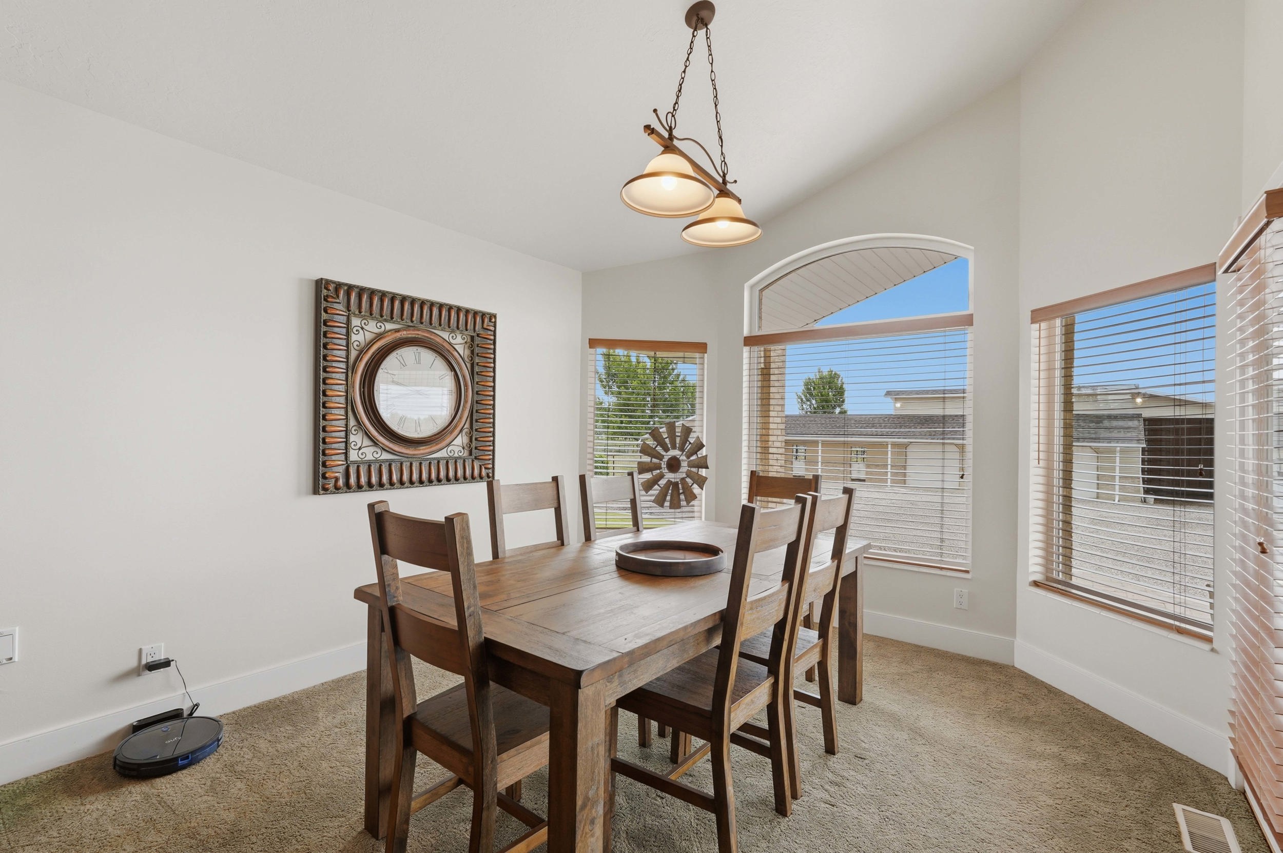 Vaulted ceiling dining area featuring an arched window, multiple windows with blinds, a bronze-finish chandelier, and neutral wall tones