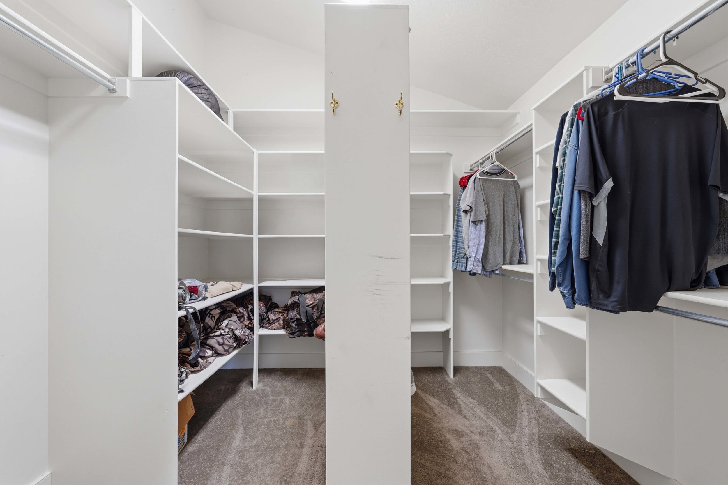 Expansive walk-in closet featuring white built-in shelving, multiple hanging rods, and a central storage column, all set on carpeted flooring