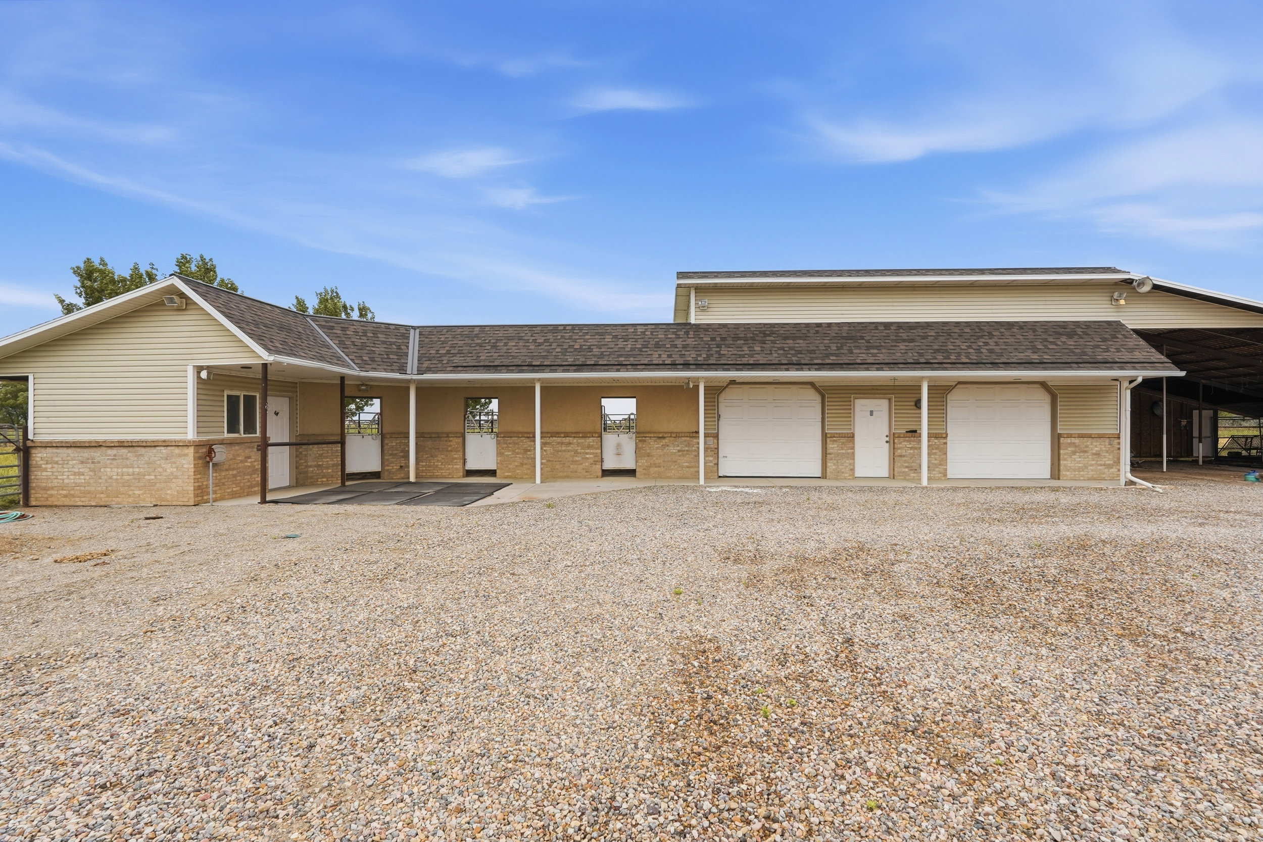 Light beige siding structure featuring a brown shingle roof, stone veneer accents, multiple entryways, and two white overhead doors