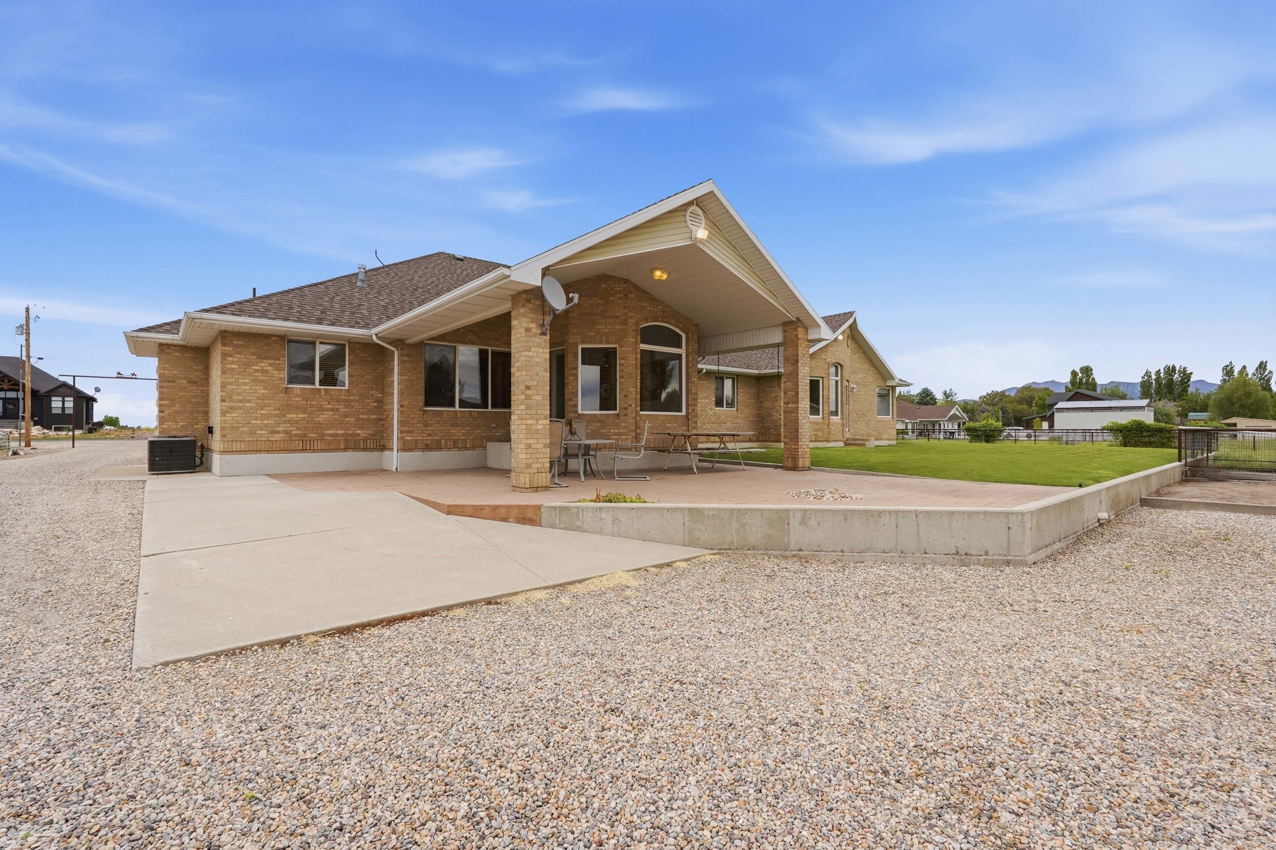 Rear exterior featuring a covered patio, expansive concrete slab, and a gravel surface