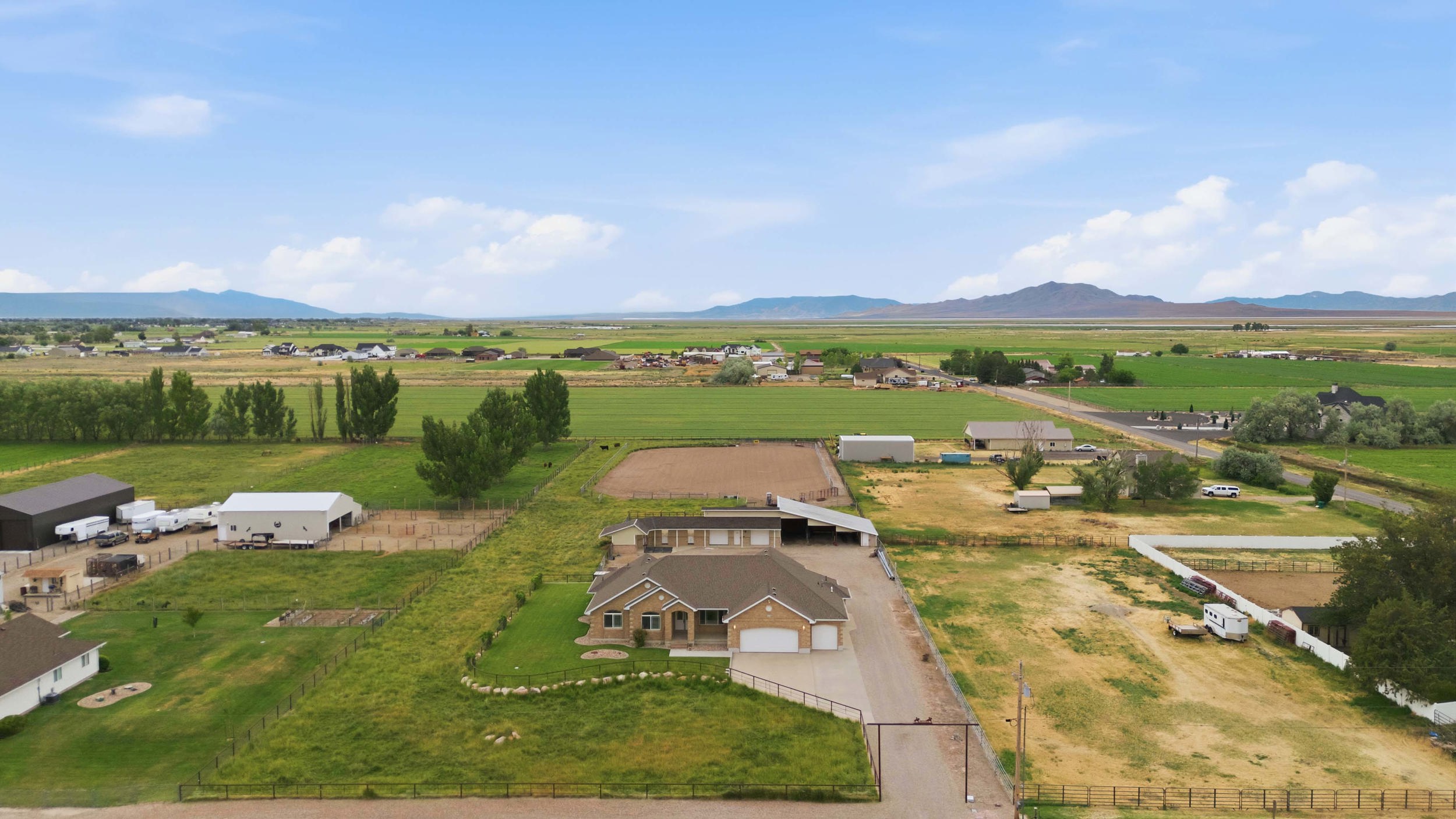 Expansive rural property featuring a main residence with attached garage, multiple outbuildings, fenced pastures, and an outdoor arena