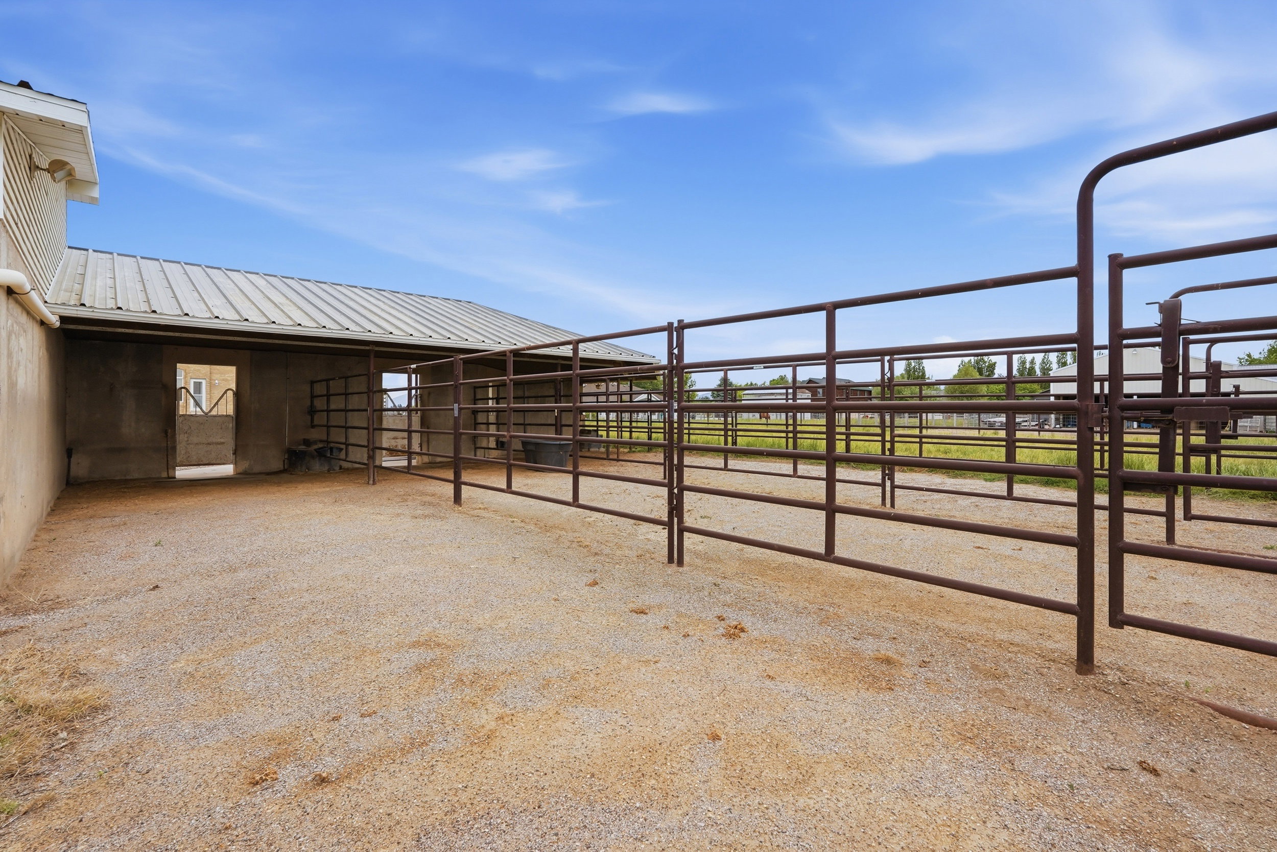 Gravel-surfaced outdoor enclosure featuring brown metal fencing and an adjacent covered structure with a metal roof