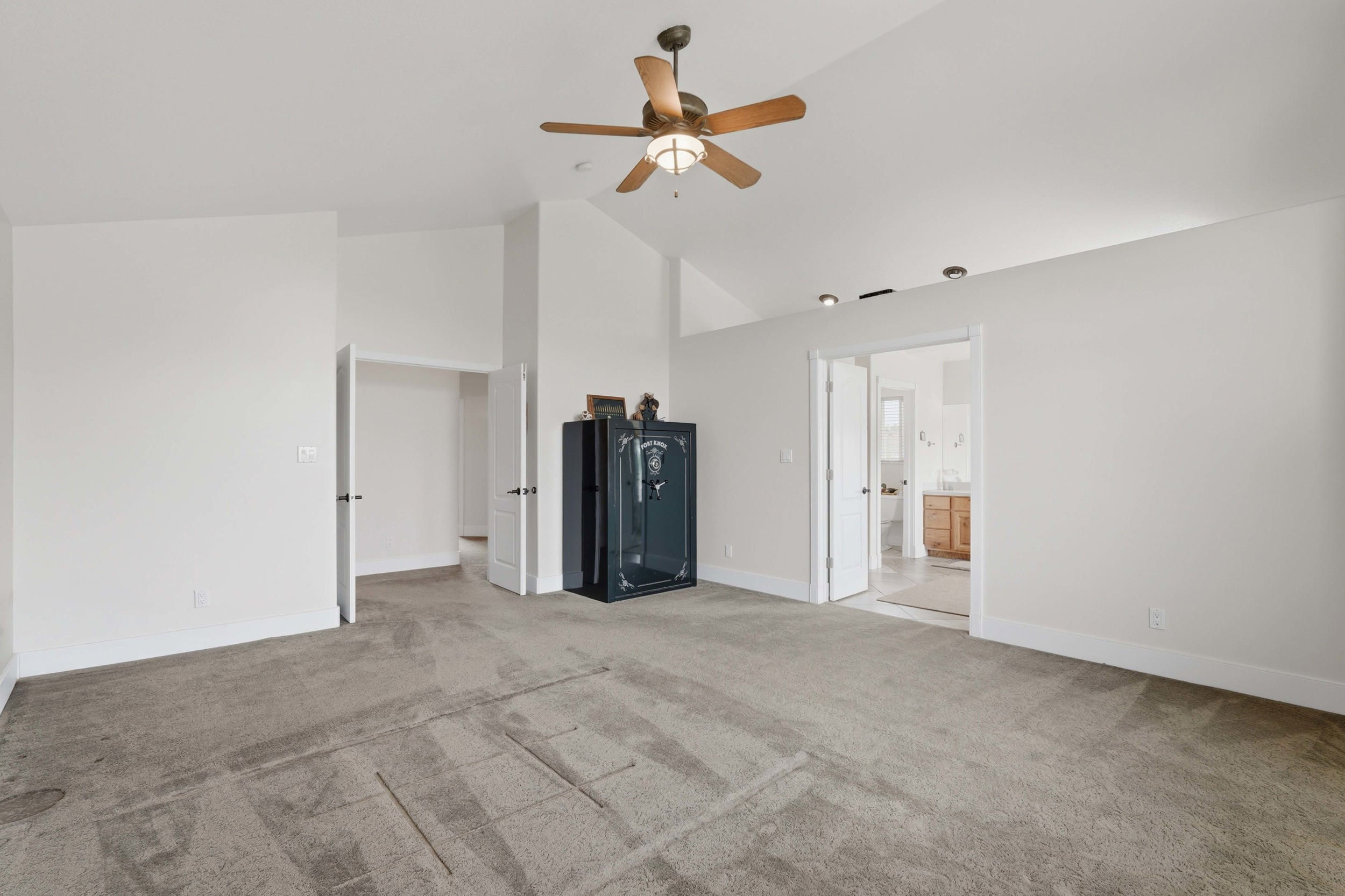 Spacious room featuring vaulted ceilings, neutral carpet flooring, and a ceiling fan with integrated lighting