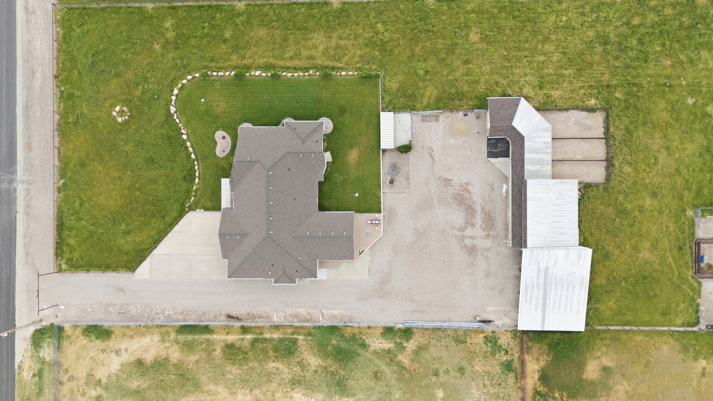 Expansive property featuring a large residence with a multi-gabled roof, extensive concrete driveway, secondary detached structure, and a blend of manicured lawn and open land