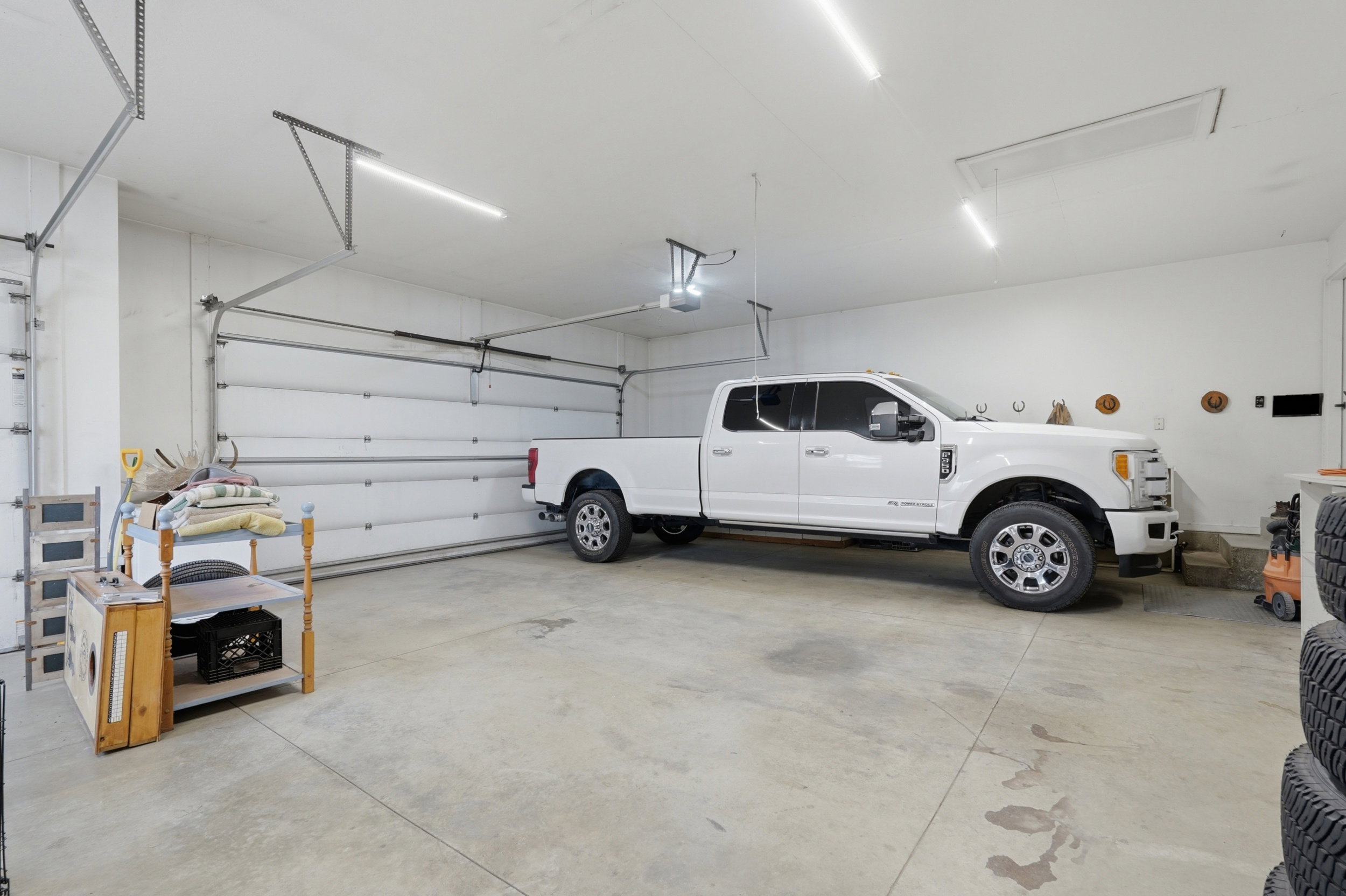 Spacious garage featuring concrete flooring, multiple overhead linear light fixtures, and two overhead garage doors