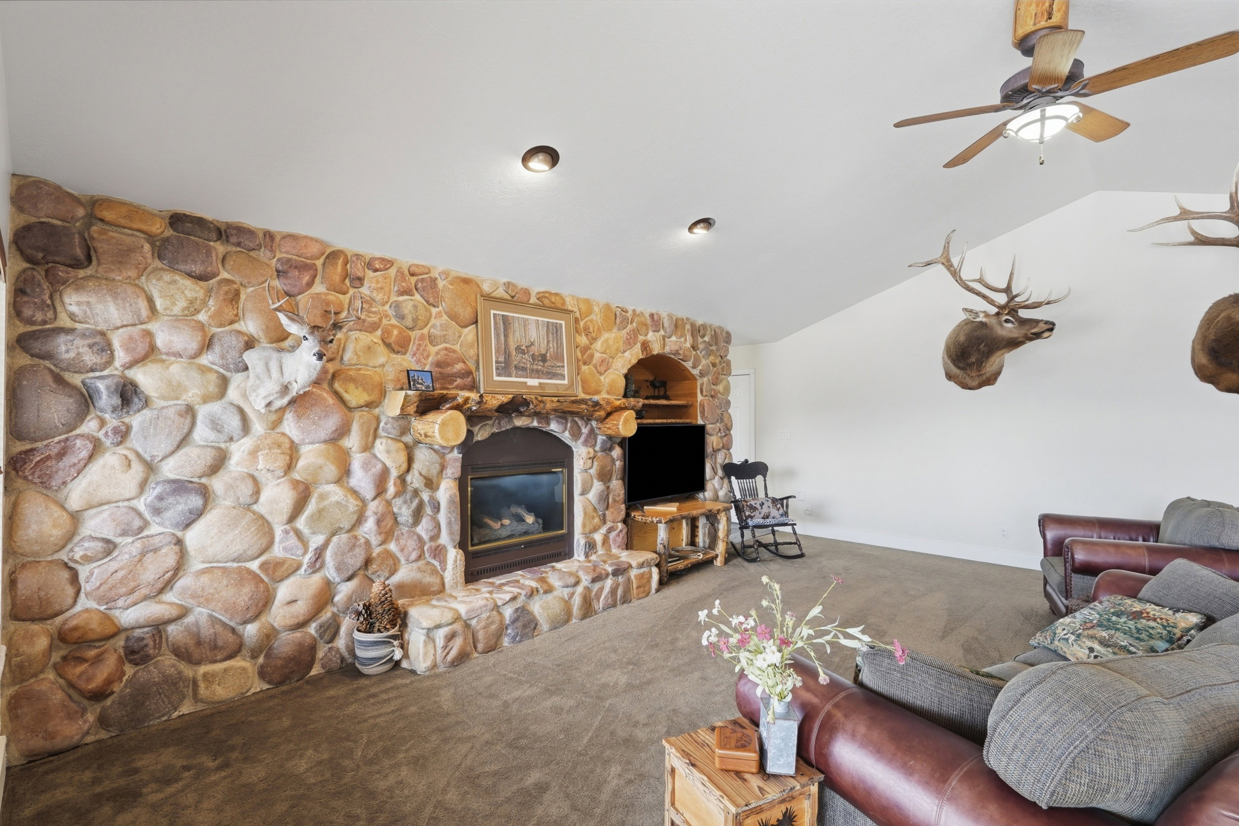 Living area featuring a stone accent wall with a built-in fireplace, vaulted white ceilings, and recessed lighting