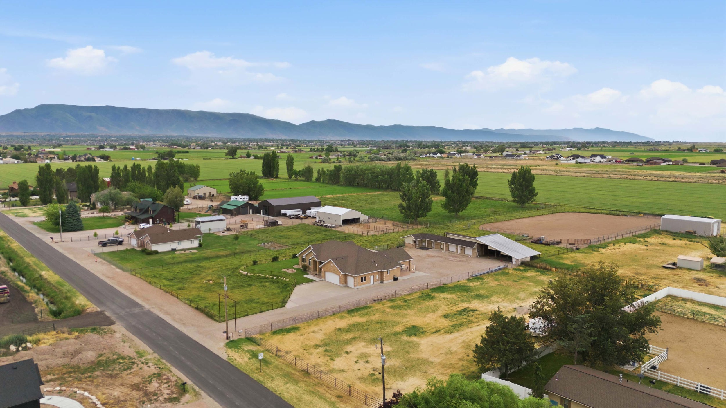 Expansive property featuring a tan-colored dwelling with an attached three-car garage, multiple outbuildings, and two fenced arenas