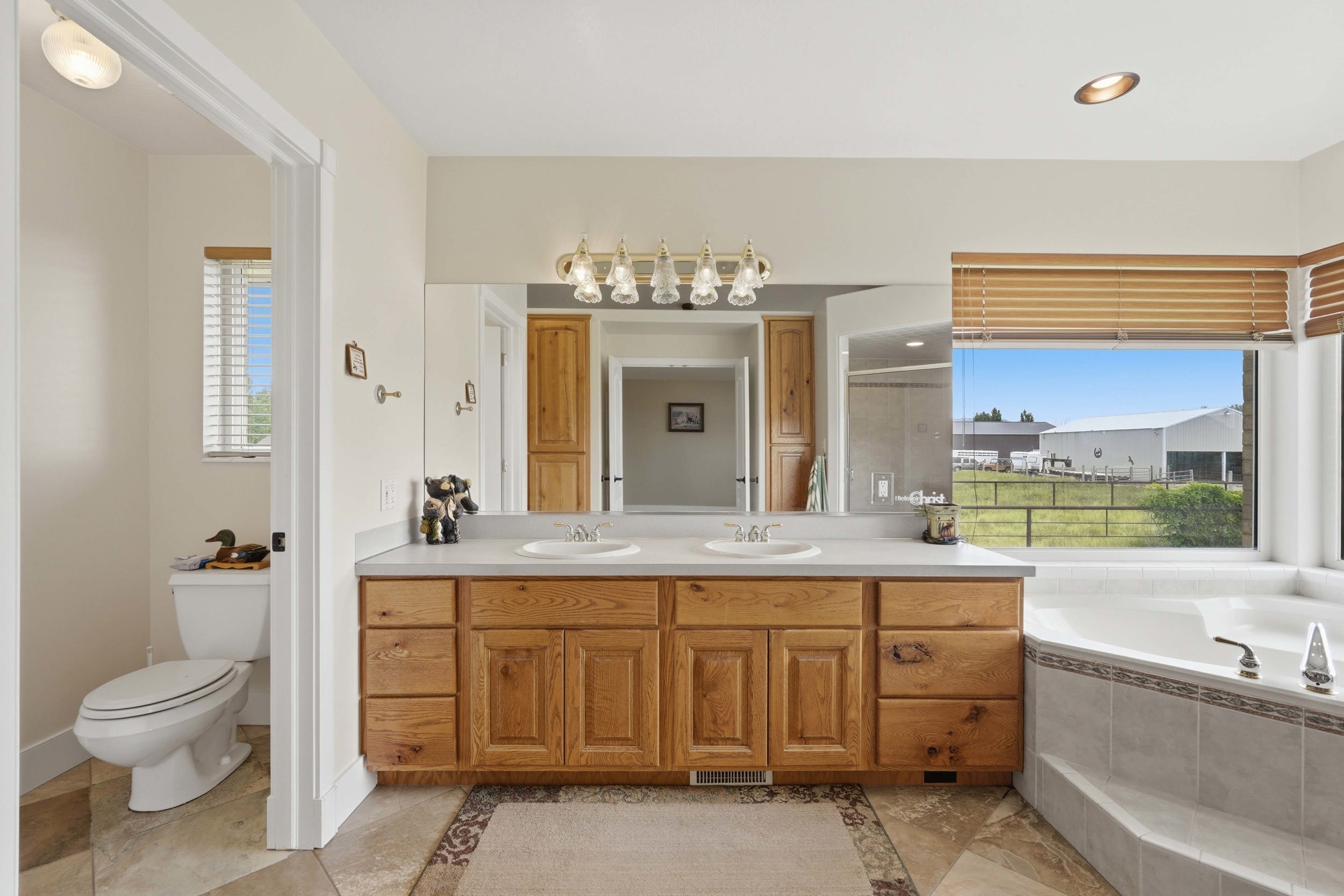 Bathroom featuring a dual vanity with wood cabinetry, a large mirror, and a built-in corner bathtub with tiled surround