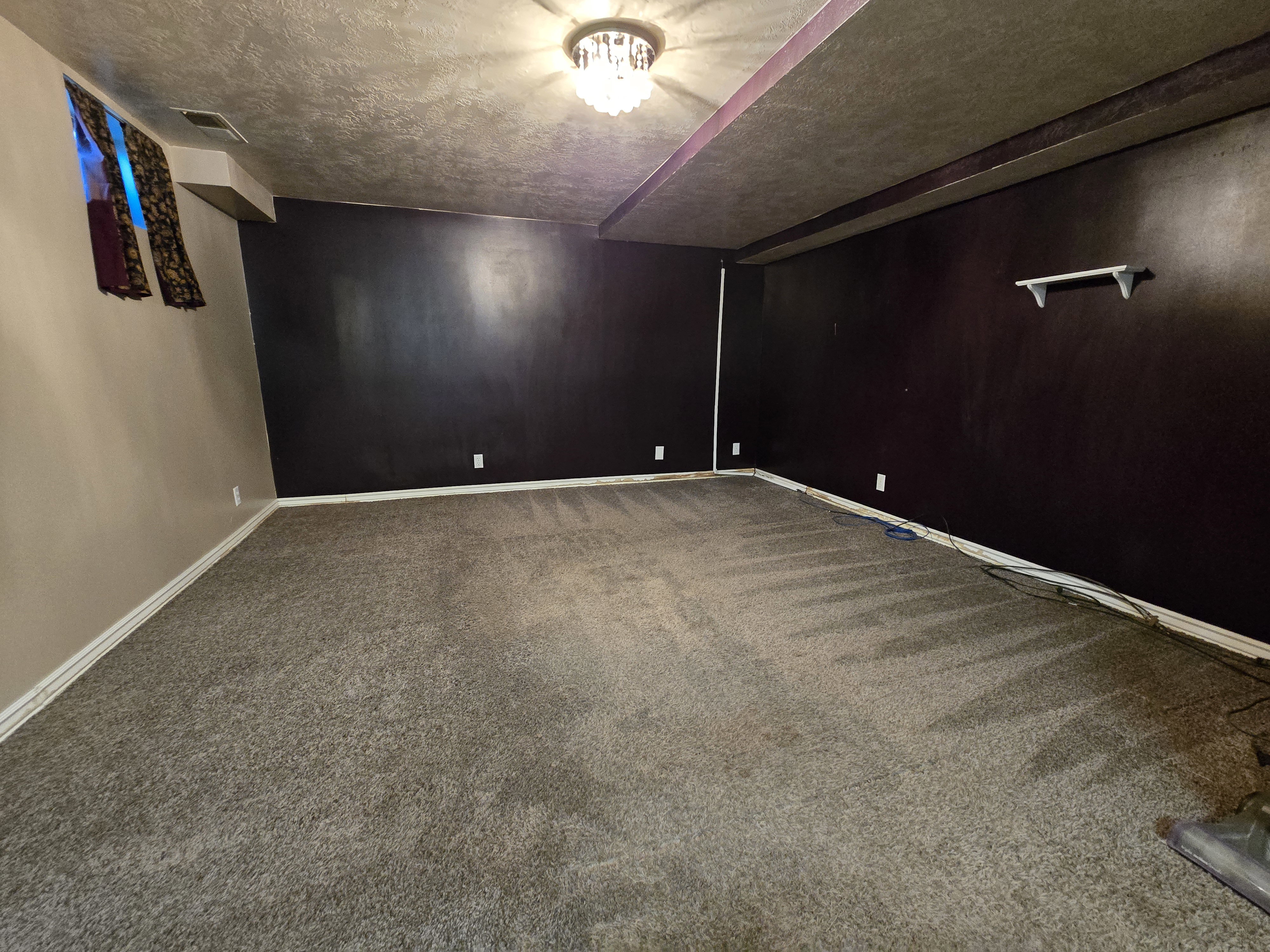 Spacious room featuring dark walls, tan walls, and grey carpet flooring
