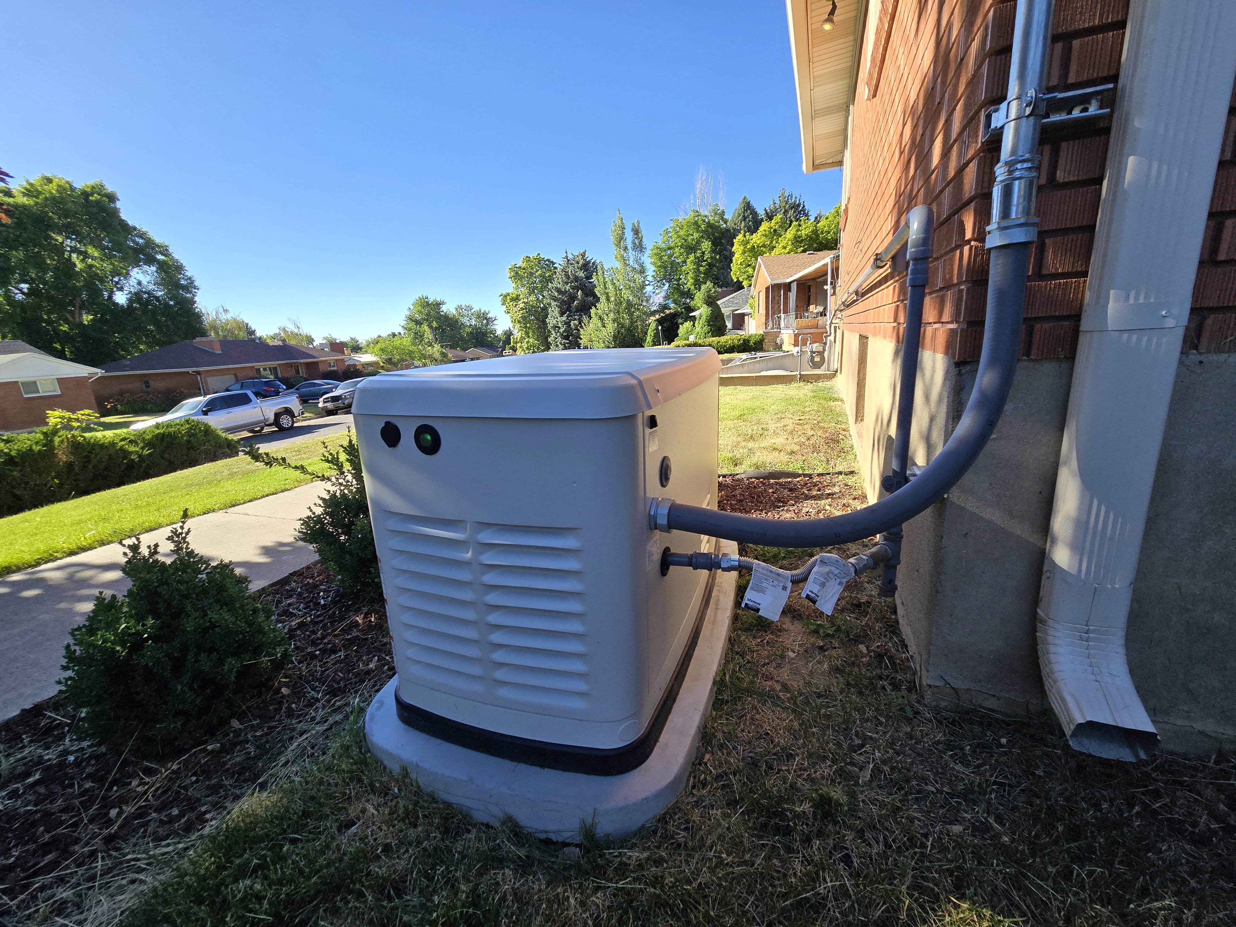 Exterior generator system installed on a concrete pad, featuring utility connections to the brick-sided structure