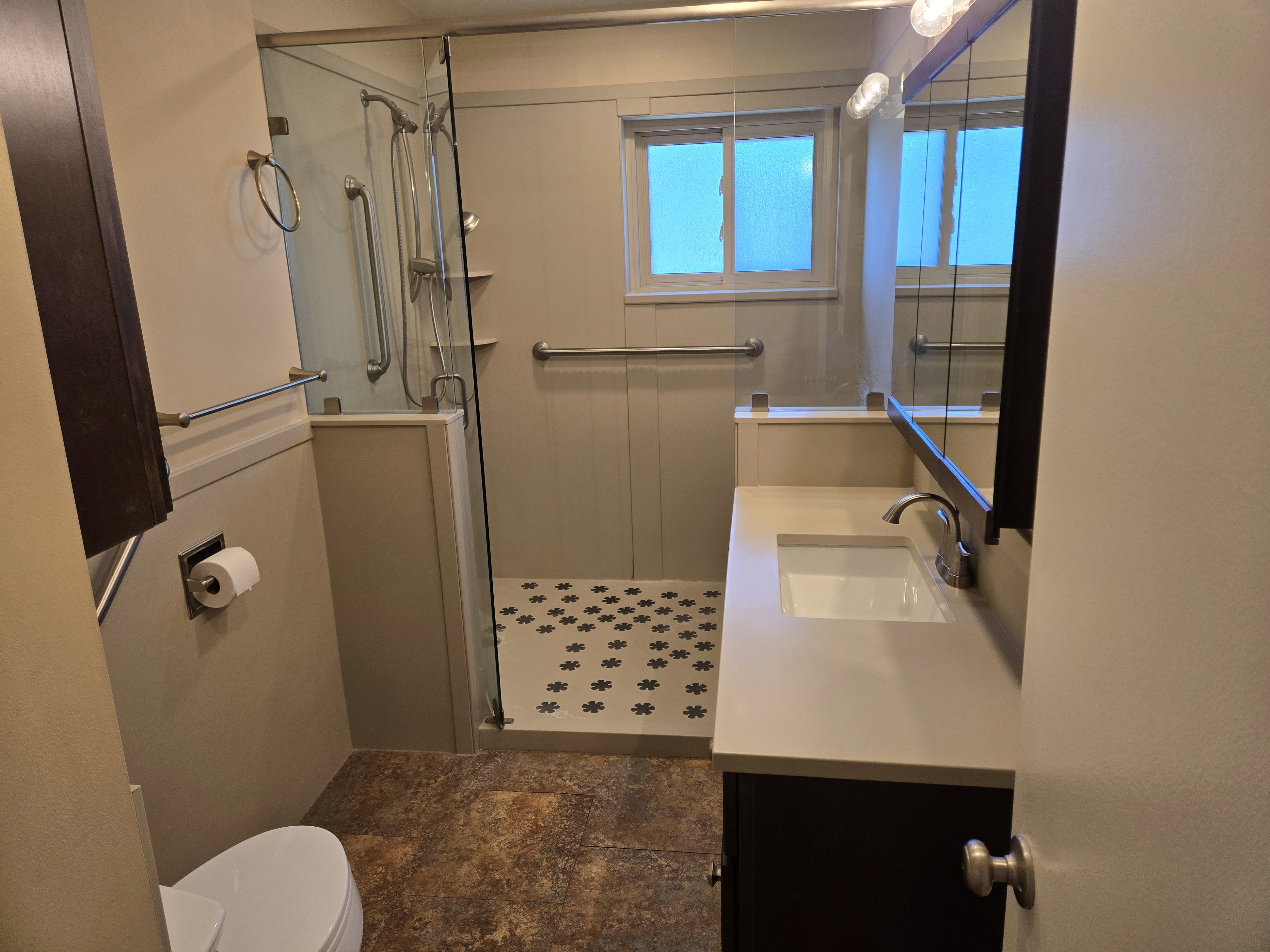 Contemporary bathroom featuring a walk-in shower with glass enclosure, decorative mosaic tile shower floor, and a single-pane window