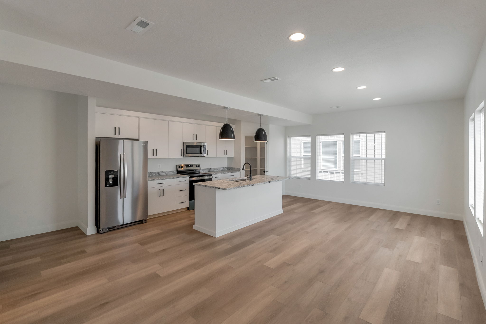 Open-concept living space featuring wood-finish flooring, recessed lighting, and multiple windows with vertical blinds