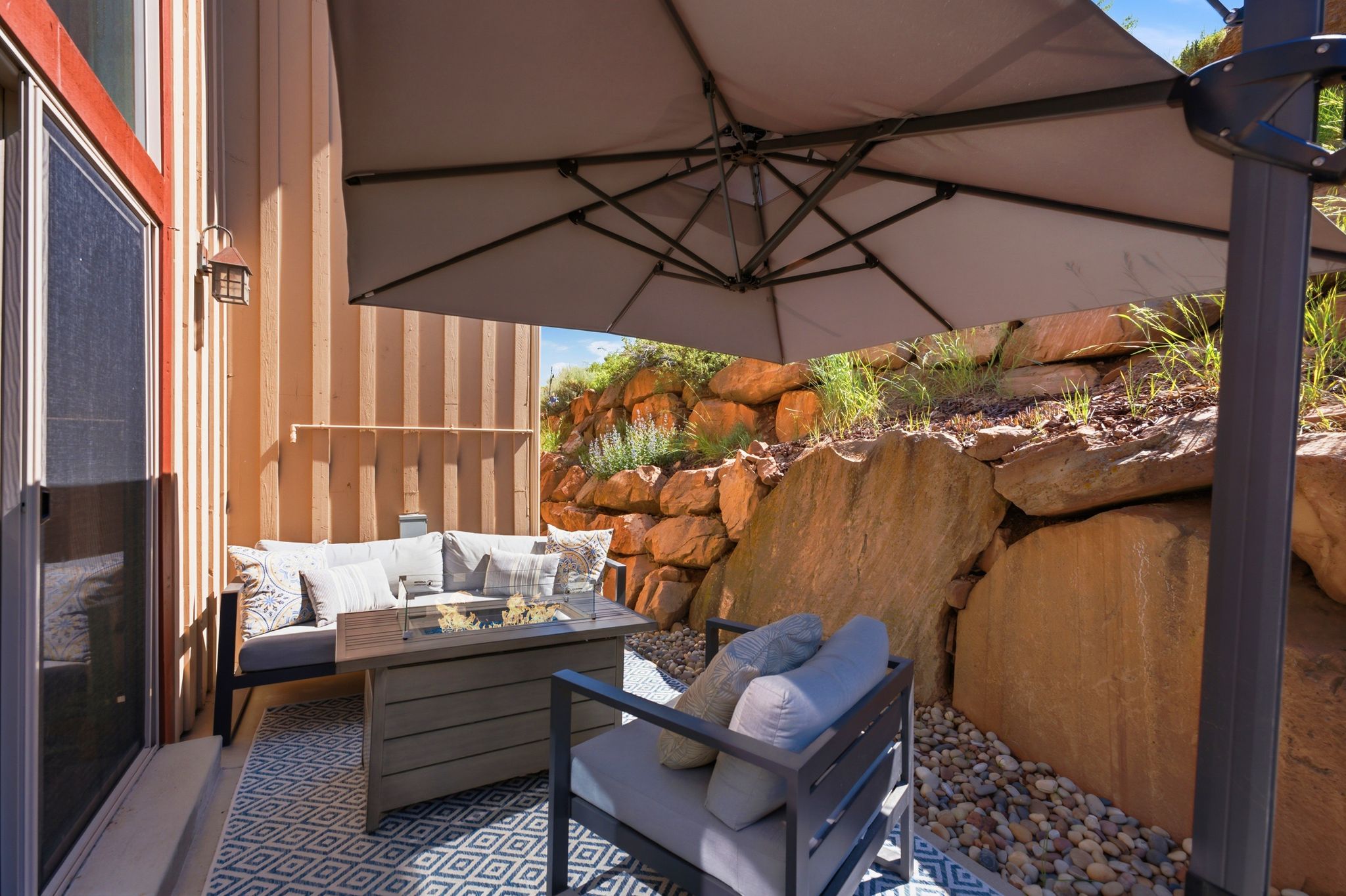 Outdoor patio with a geometric pattern rug, river rock landscaping, and natural rock retaining wall