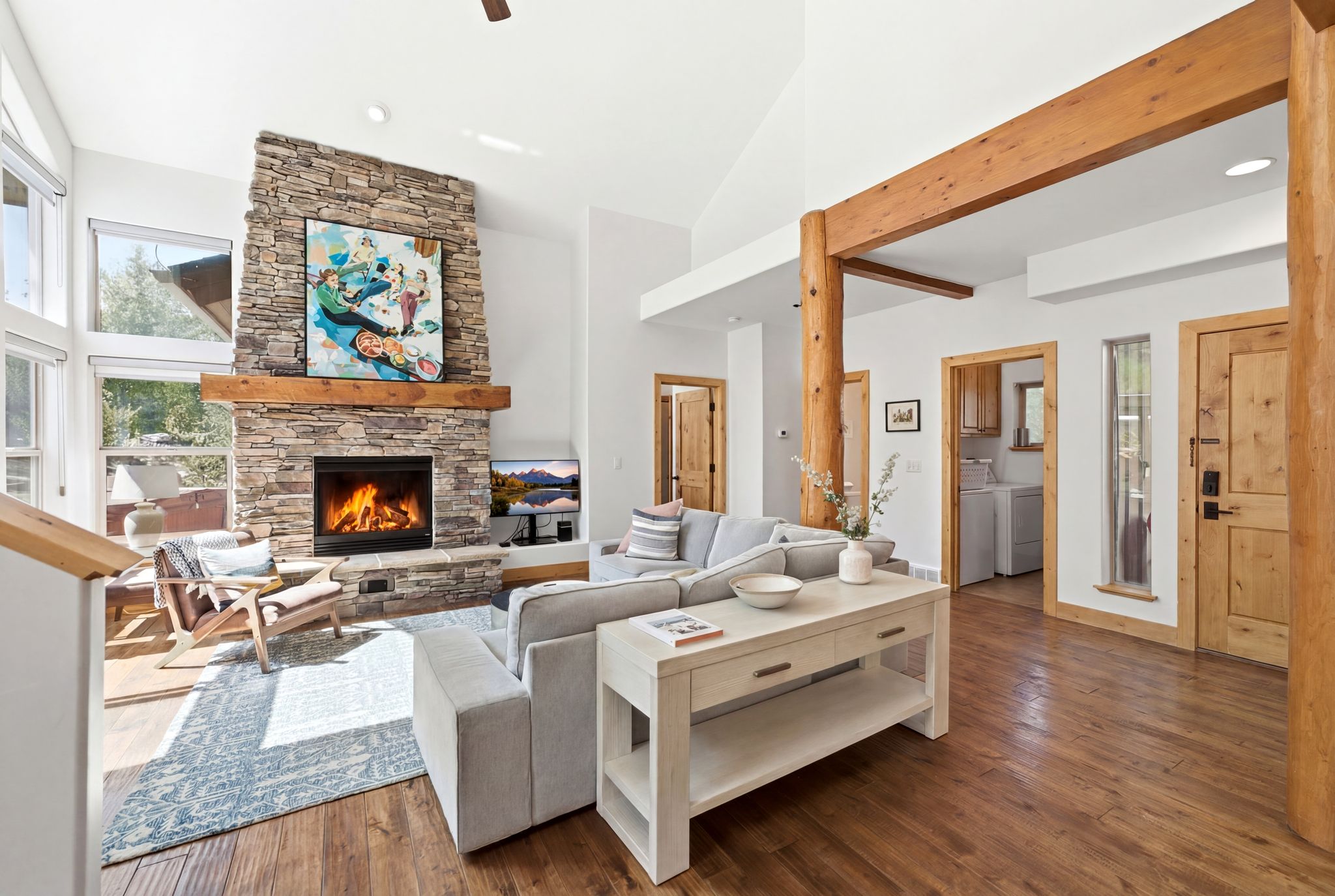 Great room featuring a floor-to-ceiling stone fireplace with a wood mantel, high vaulted ceilings, large windows, and exposed wood beams