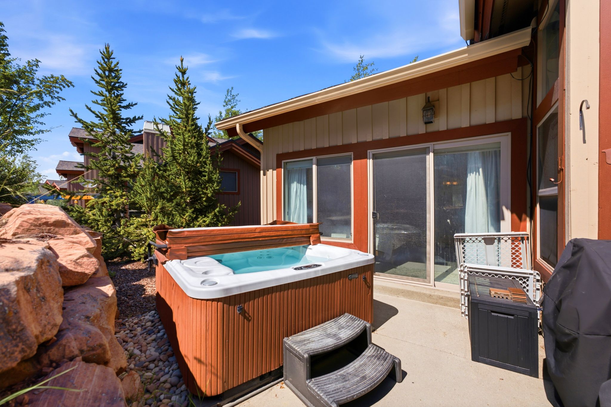 Outdoor patio featuring a built-in hot tub, concrete paving, and natural rock landscaping