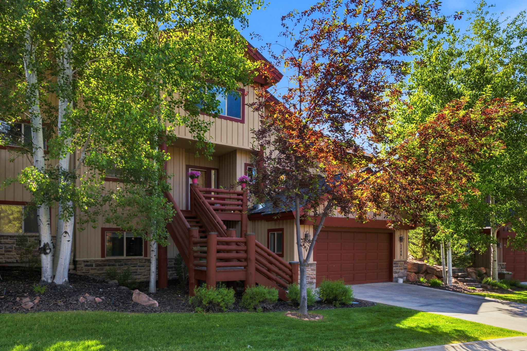 Multi-level residence featuring a stone foundation and beige siding with red trim accents