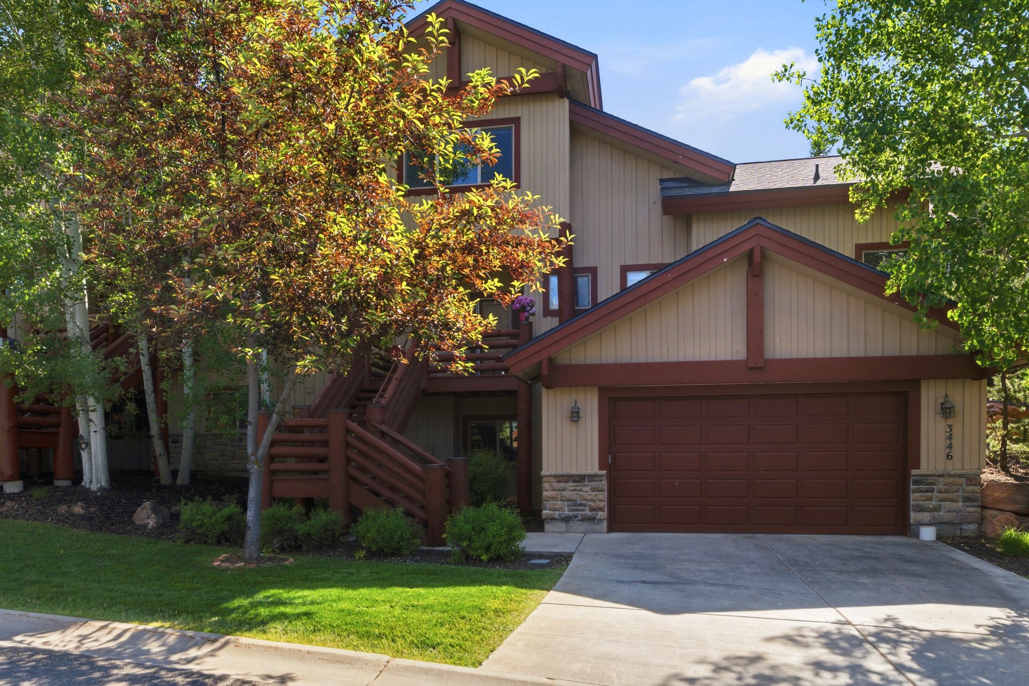 Multi-level exterior featuring tan siding with wood trim accents and stone detailing